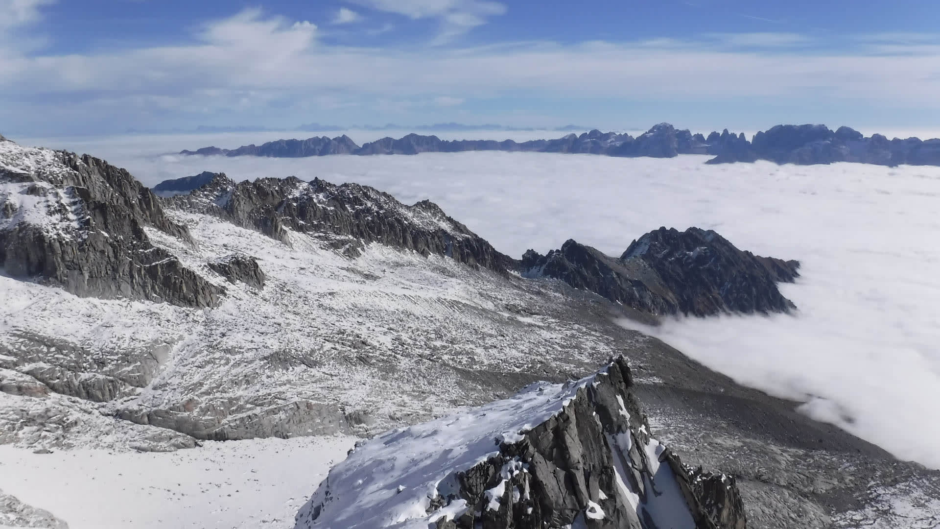 Hochtour in der Brenta: Weitwinkelpanorama über schneebedeckte Firnfelder, Felsrücken und ein geschlossenes Wolkenmeer