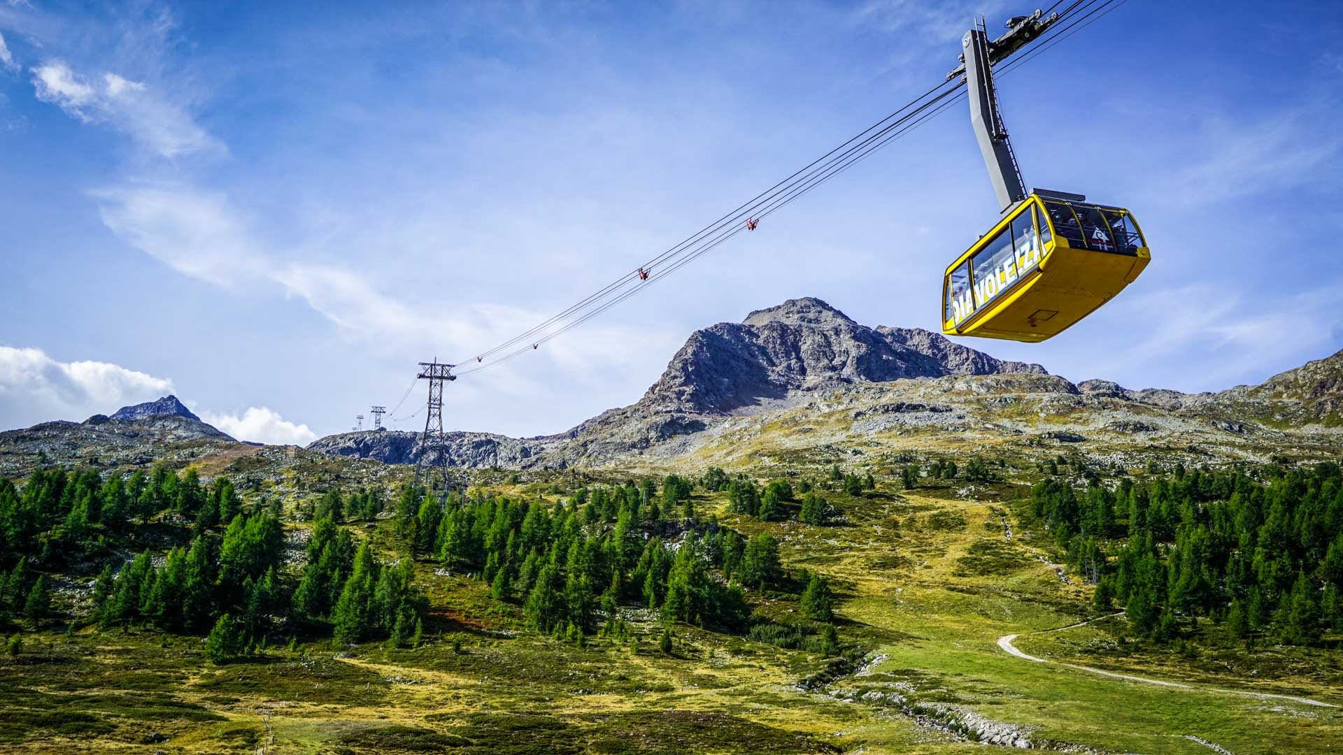 Hochtour Piz Bernina: Gelbe Gondel der Diavolezza Luftseilbahn über grüner Hochfläche mit felsigen Graten der Bernina-Alpen
