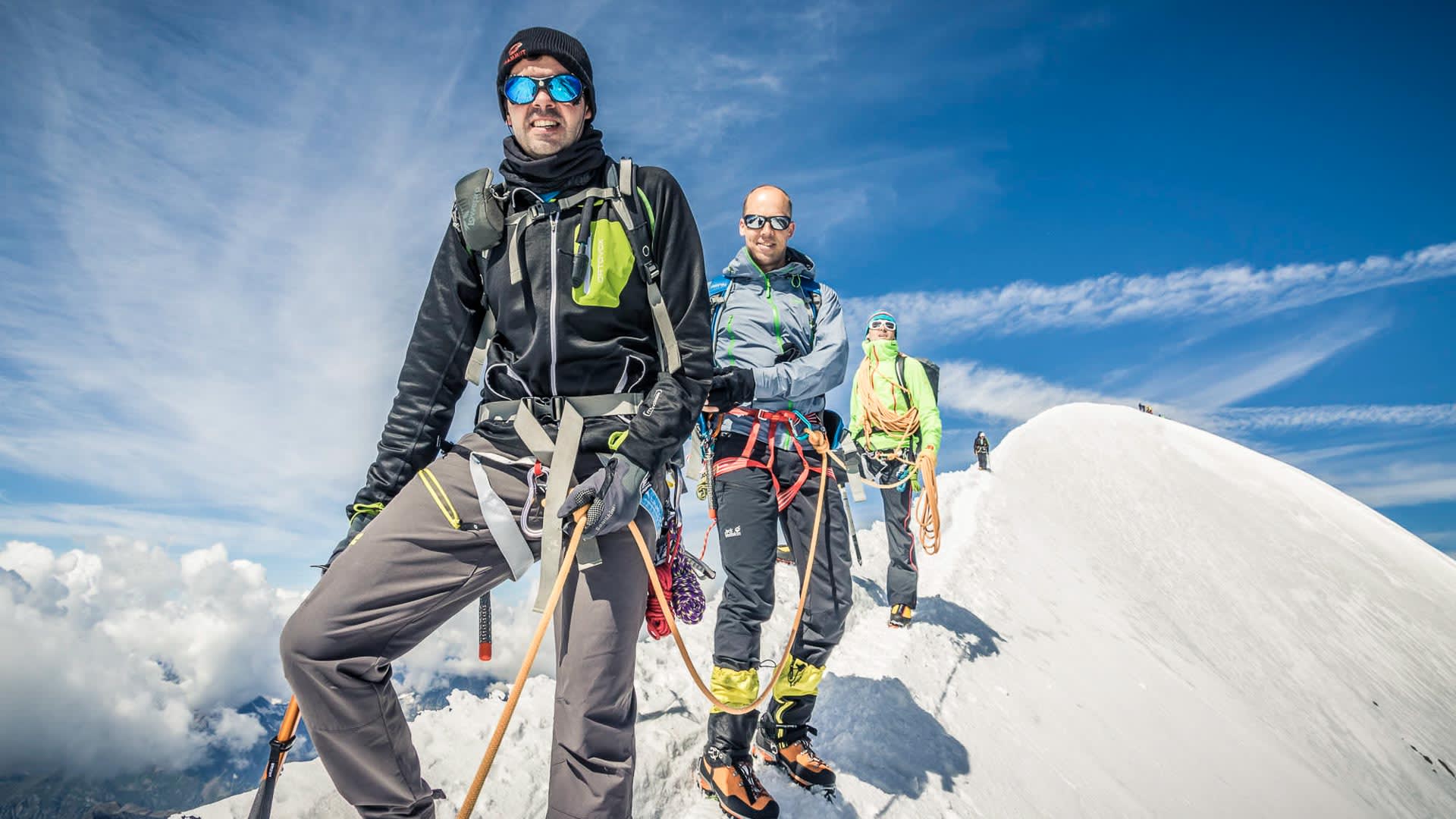 Hochtour im Wallis: Drei Bergsteiger mit Pickel und Steigeisen auf schmalem Schnee- und Eisgrat.