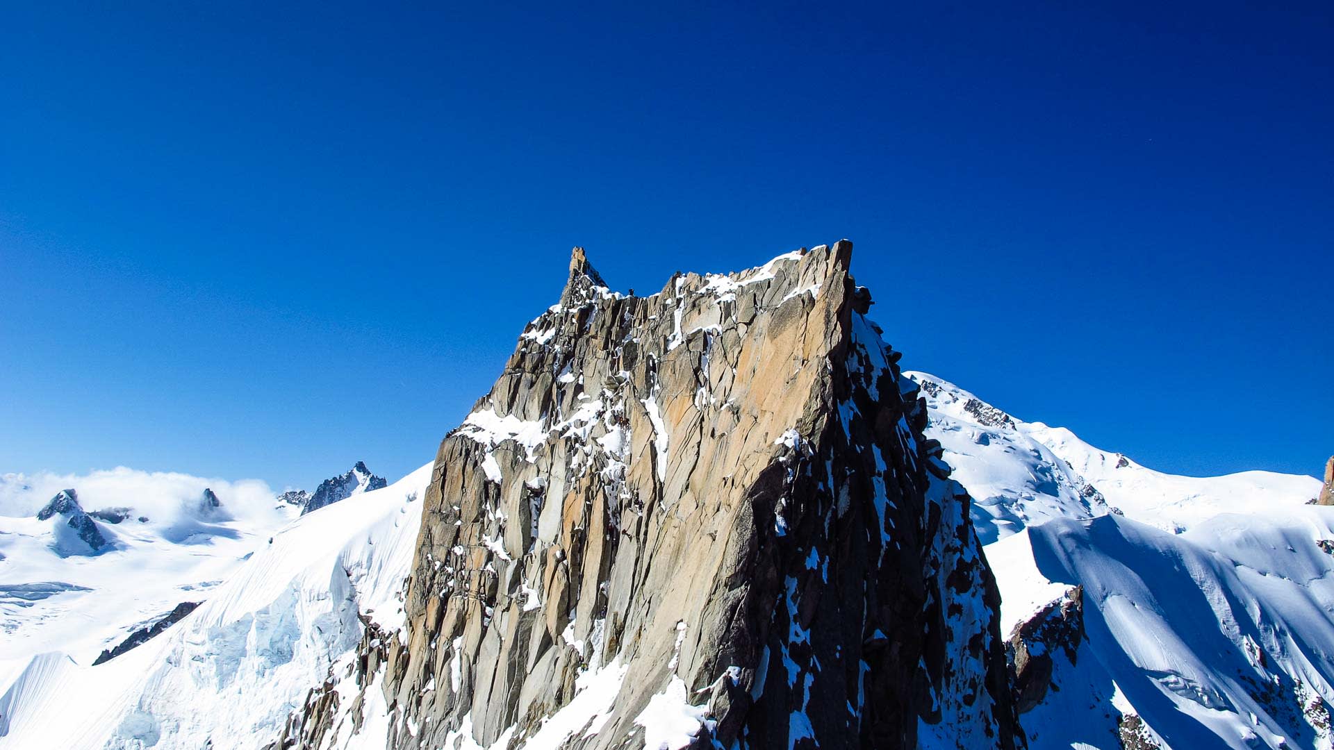 Hochtour am Chamonix-Massiv: Bergsteiger stehen auf einem zweigipfligen Granitturm über dem Gletscher.