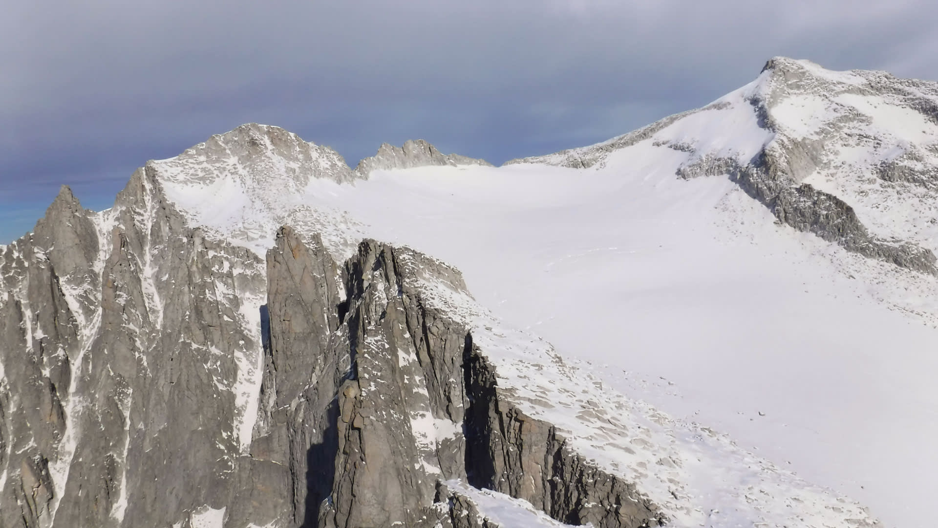 Hochtour an der Presanella: steile Felsnadeln aus geklüftetem Gestein über einem weiten Gletscherplateau im Winter.