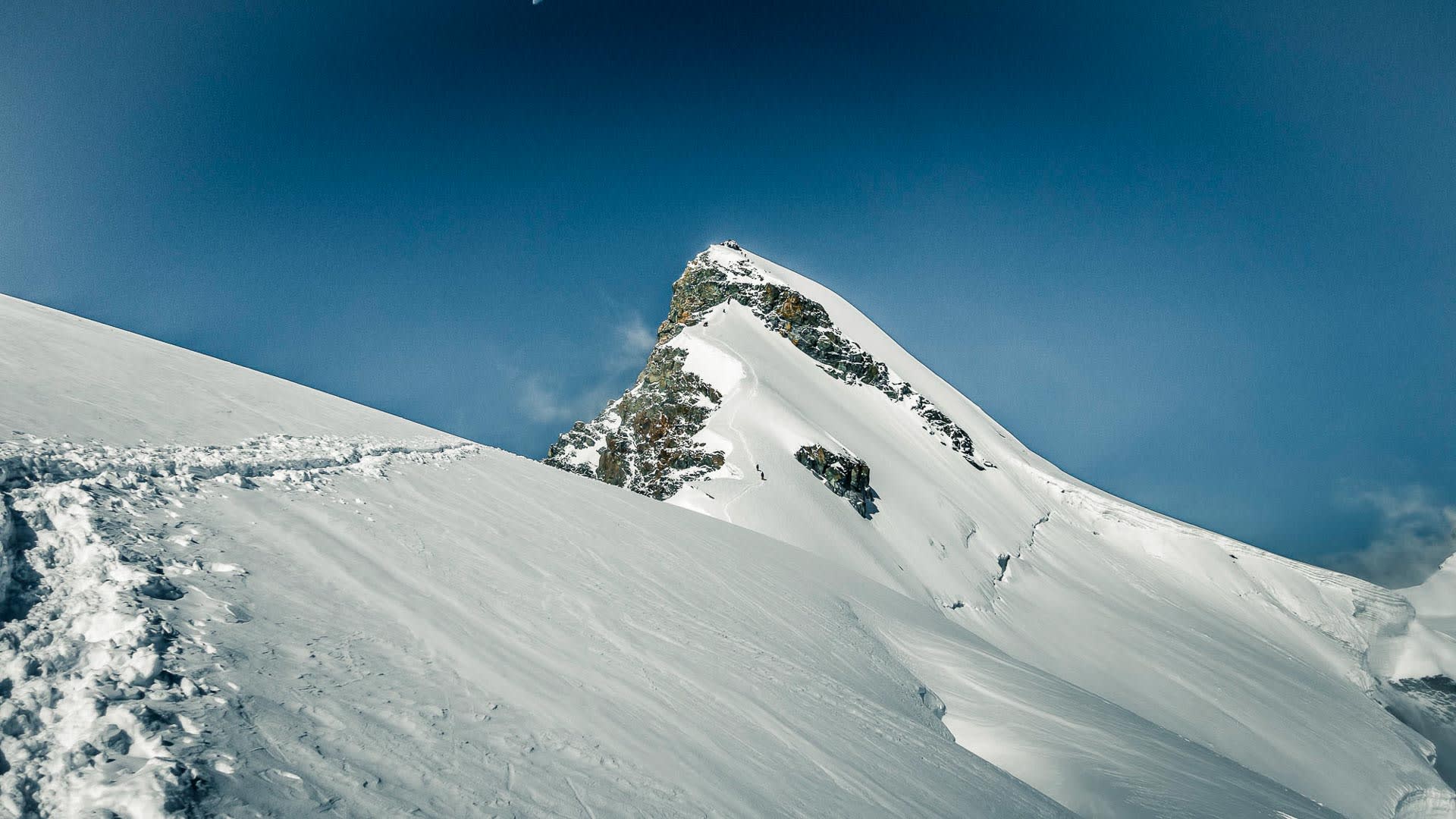 Hochtour bei Saas-Fee im Wallis: zwei Bergsteiger steigen einen verschneiten Hang zu einem Felsgipfel auf.