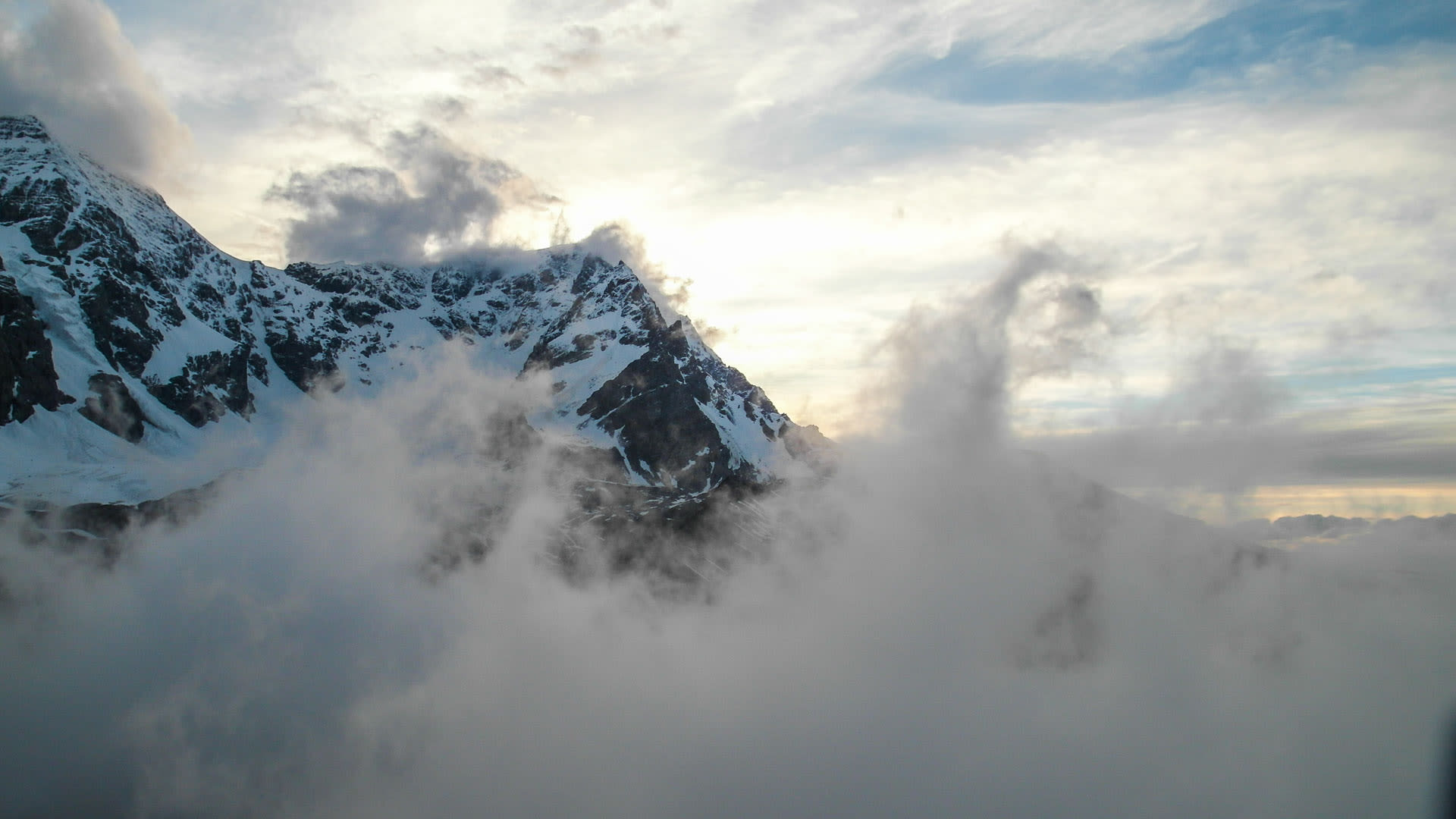 Hochtour am Ortler: Gipfelmassiv mit dunklen Felspartien ragt aus einer dichten Wolkendecke im Gegenlicht.
