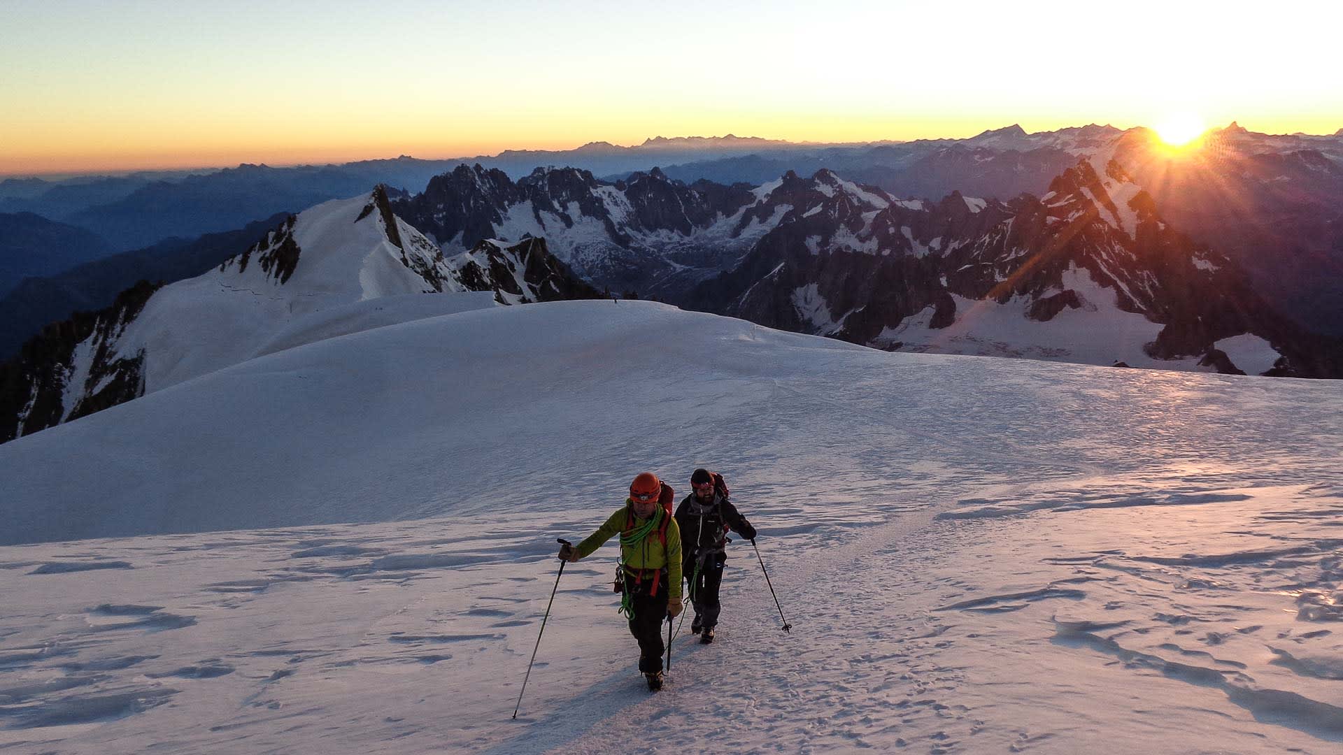 Zwei Bergsteiger mit Steigeisen und Seil steigen im Morgenrot über den Schneeplateau kurz unter dem Mont-Blanc-Gipfel auf.