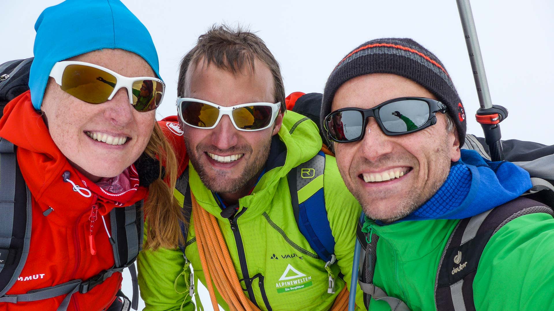 Drei Bergsteiger posieren am Gipfel des Lyskamm im Wallis mit Sonnenbrillen und Wintermützen.