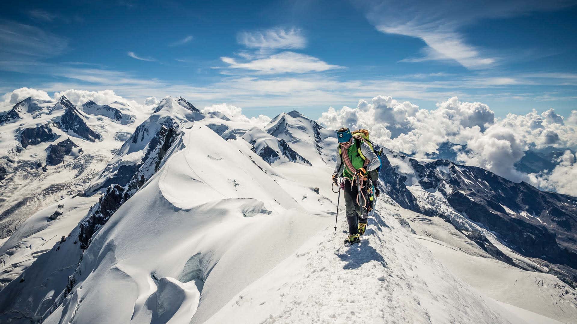 Bergsteiger mit Steigeisen und Eisstock steigt bei der Hochtour einen schneebedeckten Gipfelgrat im Wallis