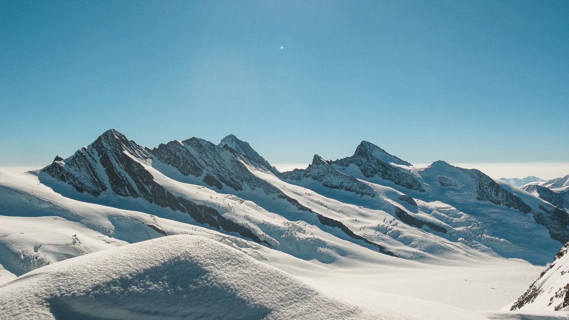 Hochtour am Finsteraarhorn: Weites Gletscherplateau mit markanter Felsgipfelkette unter wolkenlosem Himmel im Berner Oberland.