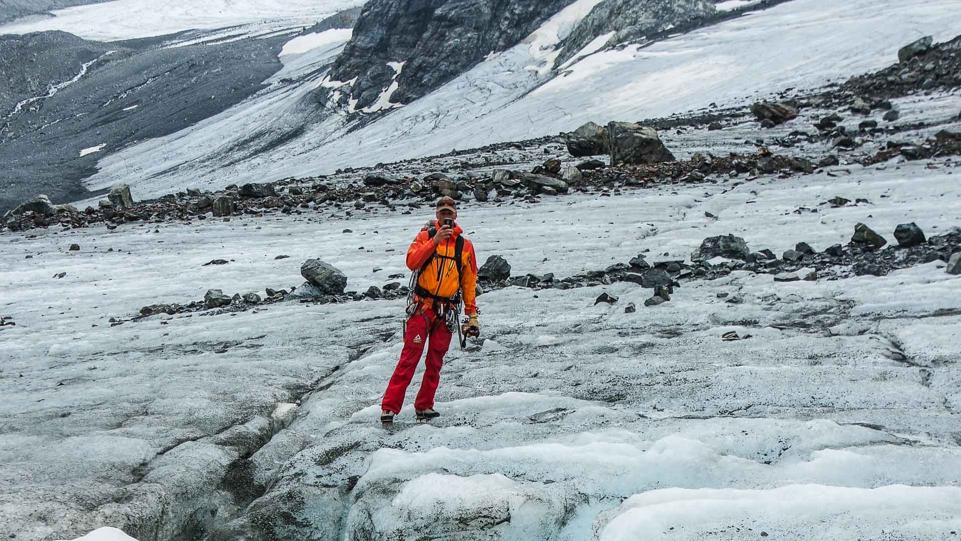 Bergsteiger in oranger Jacke mit Klettergurt auf blankem Gletschereis am Piz Buin im Sommer.