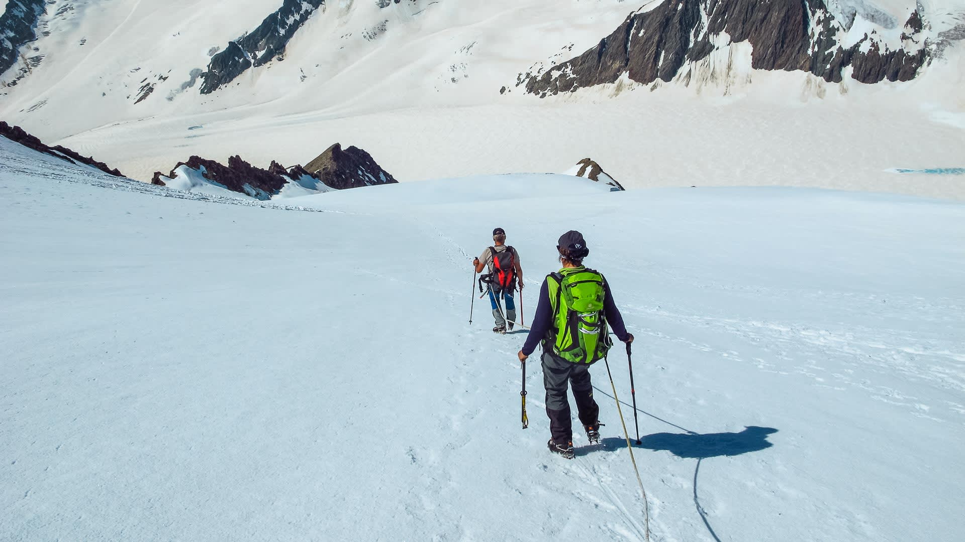 Zwei Bergsteiger mit Steigeisen traversieren einen Firn- und Gletscherhang am Ortler im Sommer.