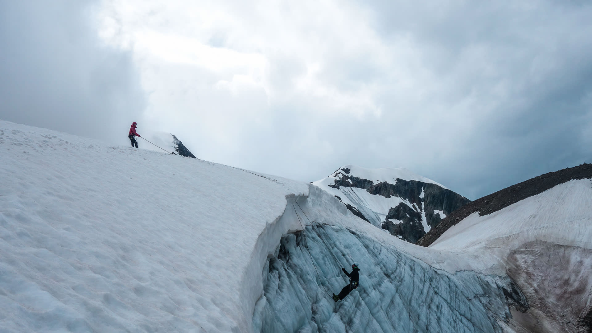 Hochtour Gletscherkurs Schweiz: Bergsteiger seilt sich an blauer Eiswand einer Gletscherspalte ab, zweite Person sichert