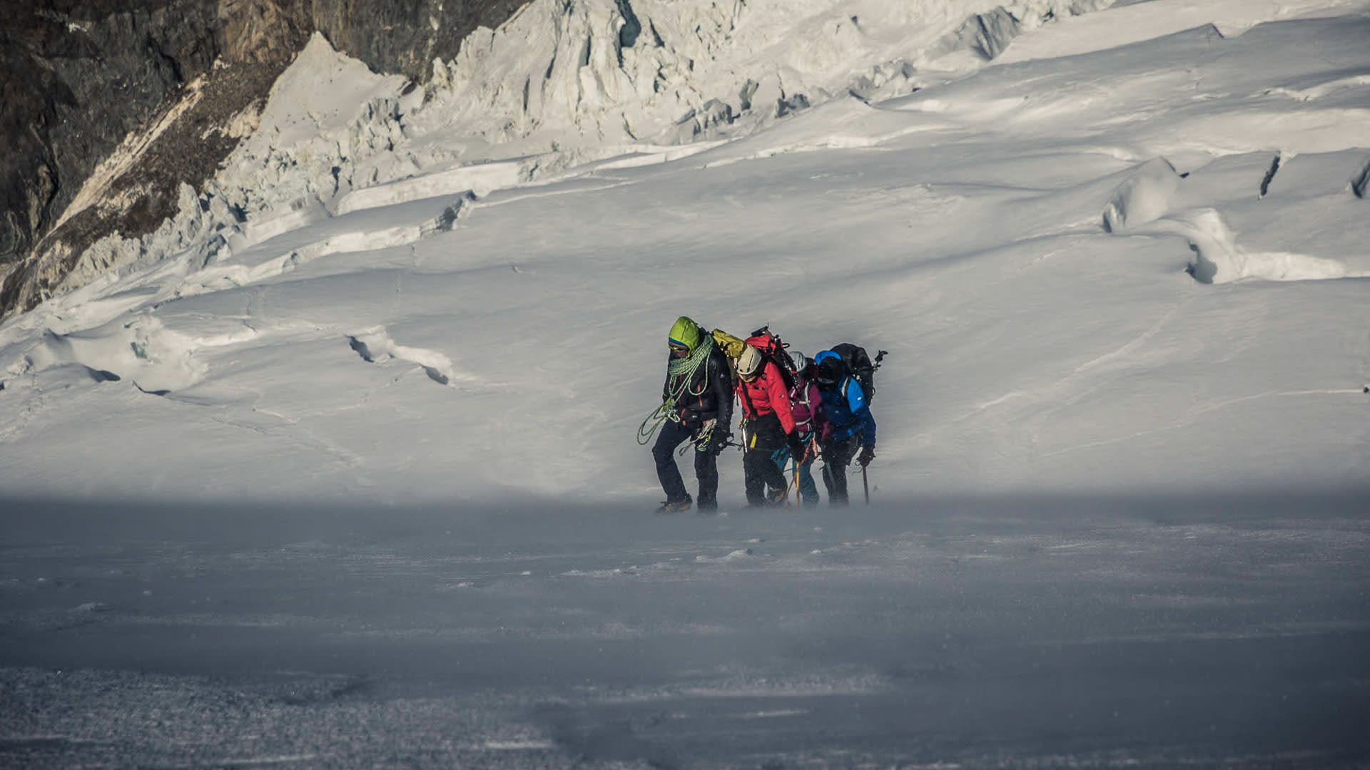 Drei Bergsteiger mit Rucksäcken und Hochtouren-Ausrüstung auf dem Gletscherplateau des Gran Paradiso bei Schneetreiben.