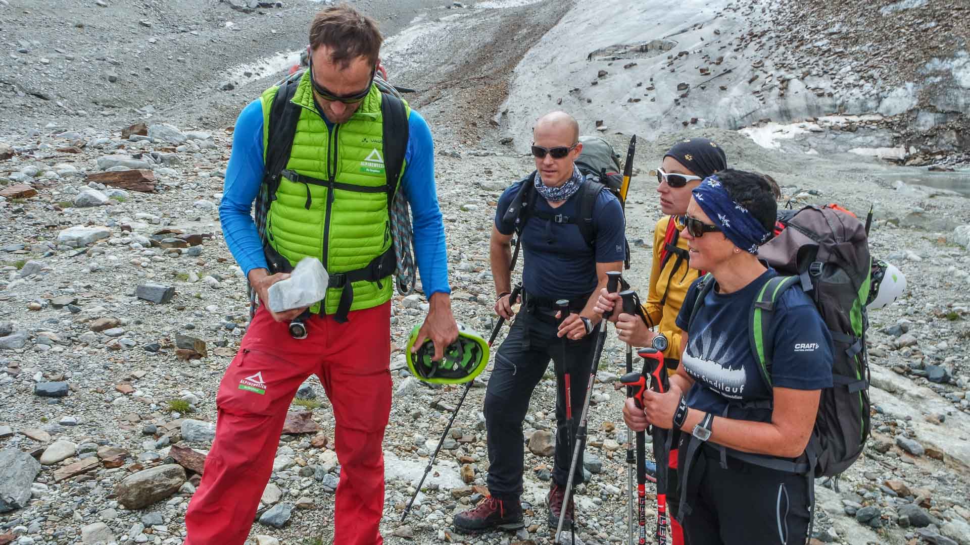 Vier Bergsteiger machen Pause am schottrigen Gletscherrandgelände beim Piz Buin in der Silvretta.