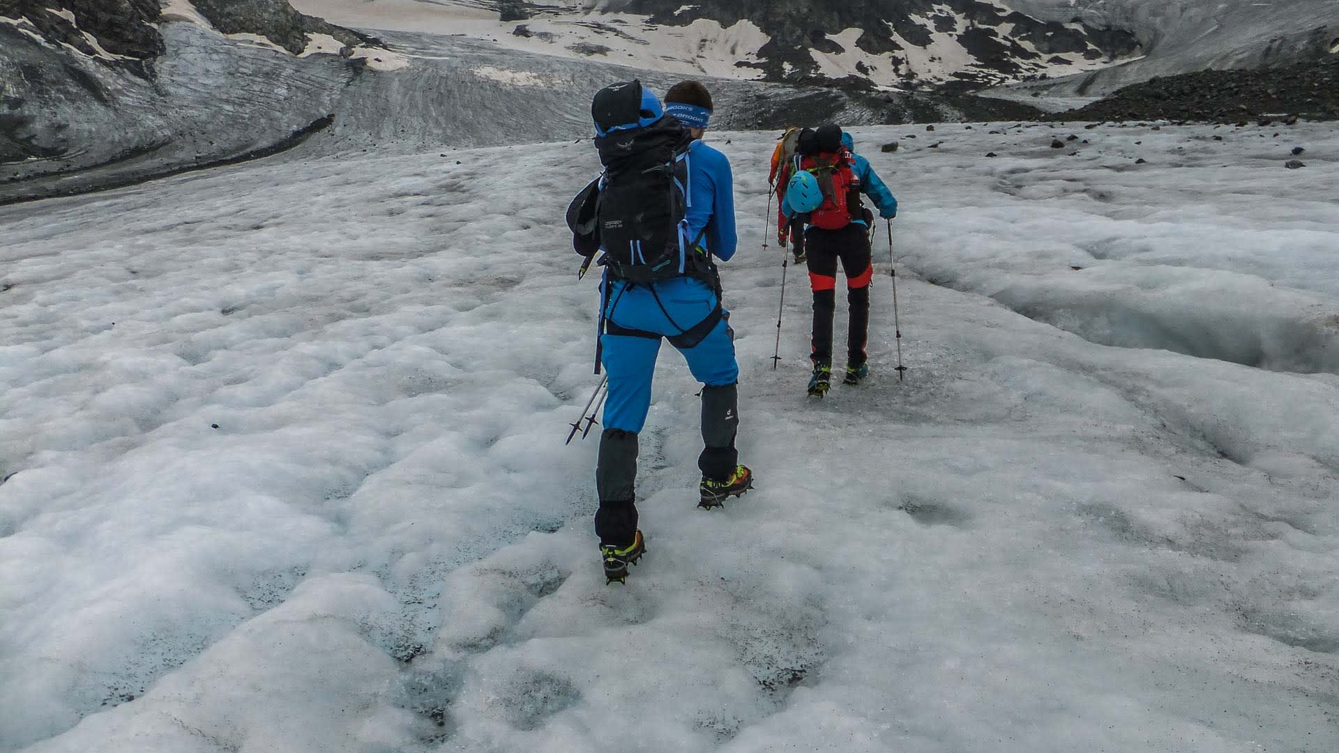 Hochtour Piz Buin: Zwei Bergsteiger mit Steigeisen und Stöcken traversieren einen Gletscher in Richtung Felsgrat.