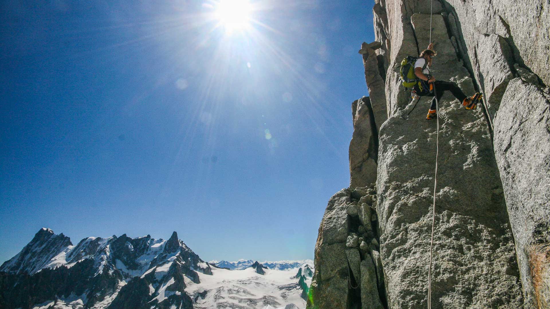 Hochtour am Mont Blanc: Bergsteiger klettert mit Gurt und Seil eine senkrechte Granitfelswand vor Gletscherpanorama.