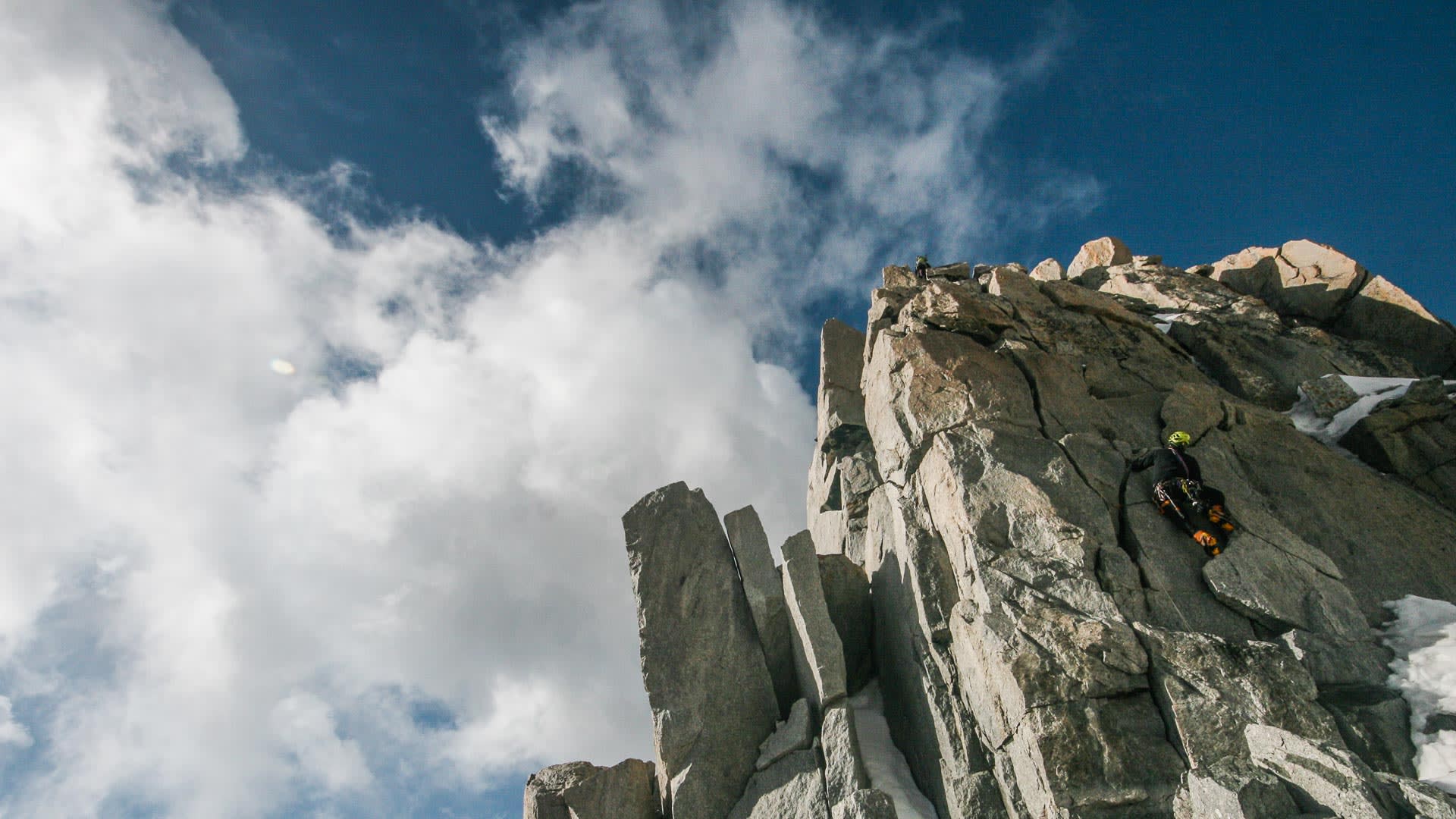 Zwei Bergsteiger klettern und sichern an steiler Granitfelswand mit Schneeresten im Mont-Blanc-Massiv.