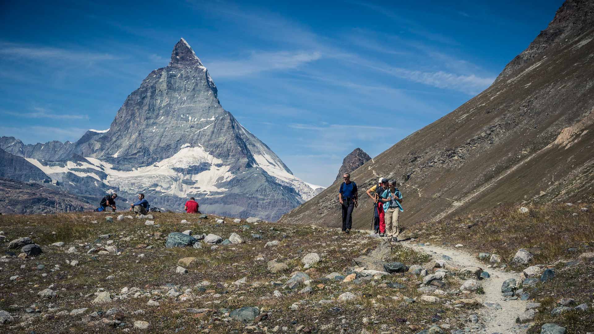 Drei Bergsteiger steigen bei einer Hochtour am Matterhorn einen Schotterweg in der hochalpinen Zone der Walliser Alpen ab