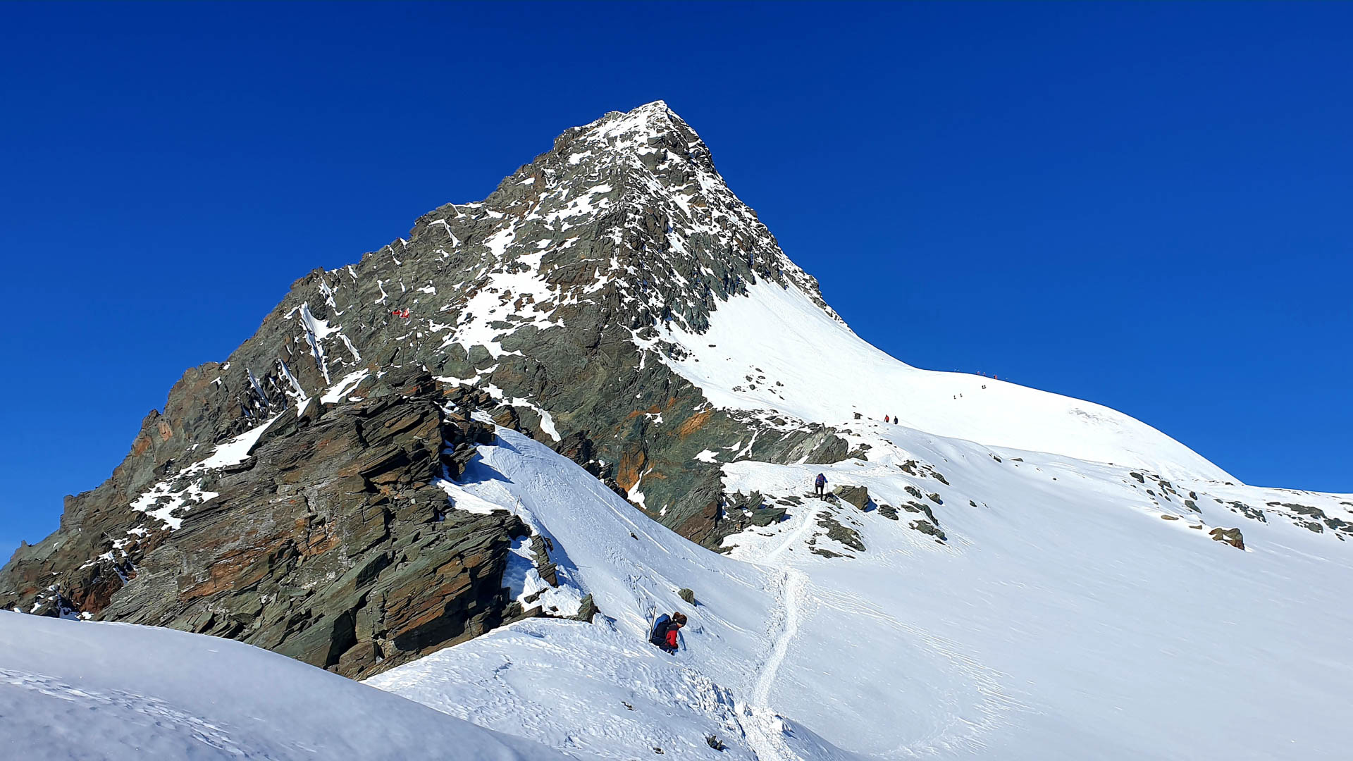 Hochtour am Großglockner-Normalweg: Bergsteiger steigen über die Schneespur unterhalb des pyramidenförmigen Gipfels auf.