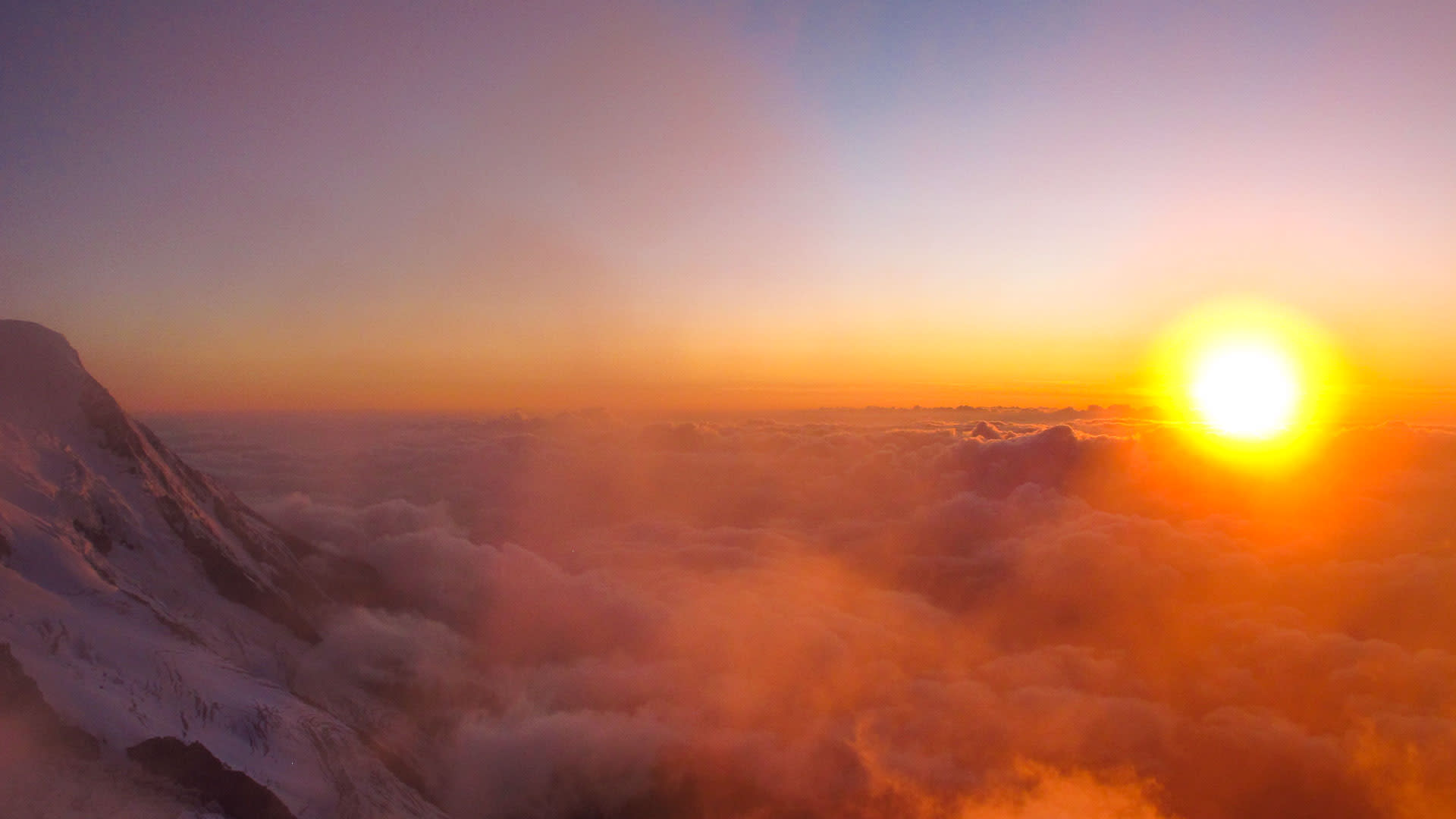 Hochtour an der Cosmique Hütte: Blick über ein Wolkenmeer mit schneebedecktem Berghang und Sonnenaufgang im Mont-Blanc-Massiv.
