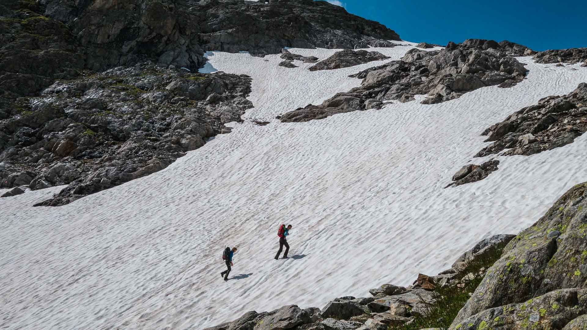 Zwei Bergsteiger queren im Hochtourenkurs einen ausgedehnten Firnhang zwischen Felsrippen im Hochgebirge.