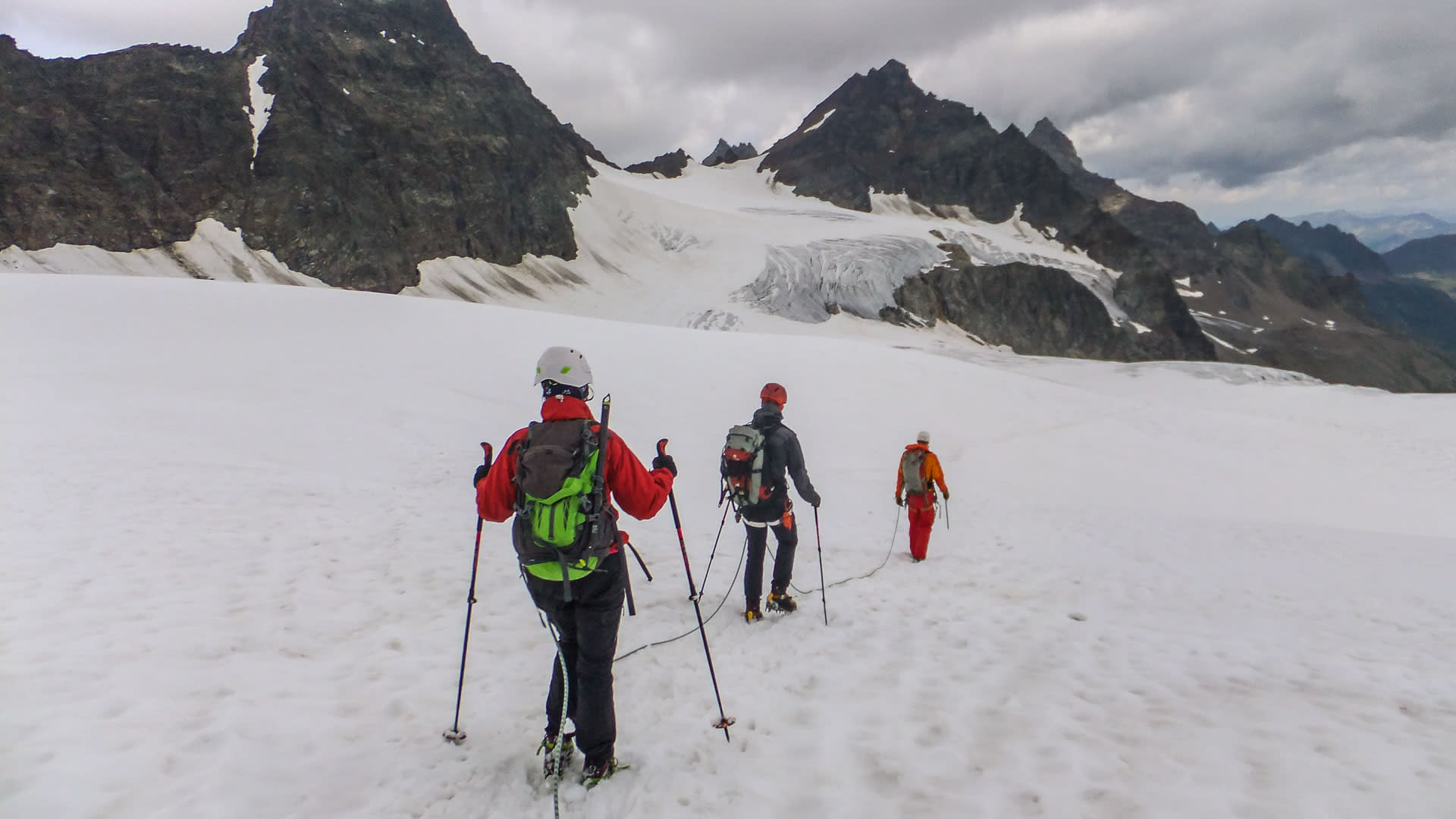 Hochtour Piz Buin: Drei Bergsteiger in Seilschaft mit Steigeisen und Stöcken steigen über ein Schneefeld zum Gletscher auf.
