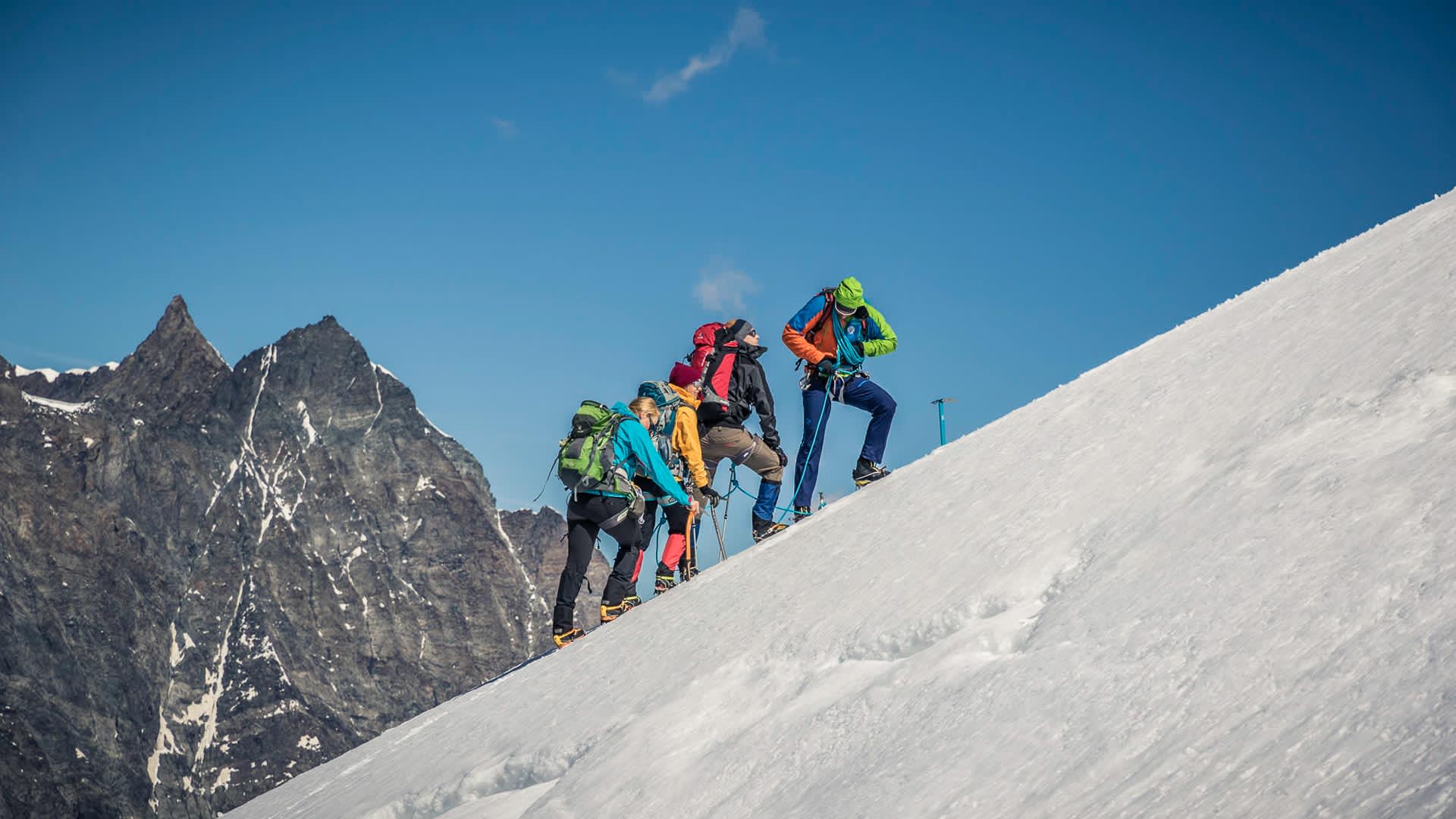 Hochtour im Wallis: Vier Bergsteiger steigen am Seil gesichert einen steilen Schneehang auf.