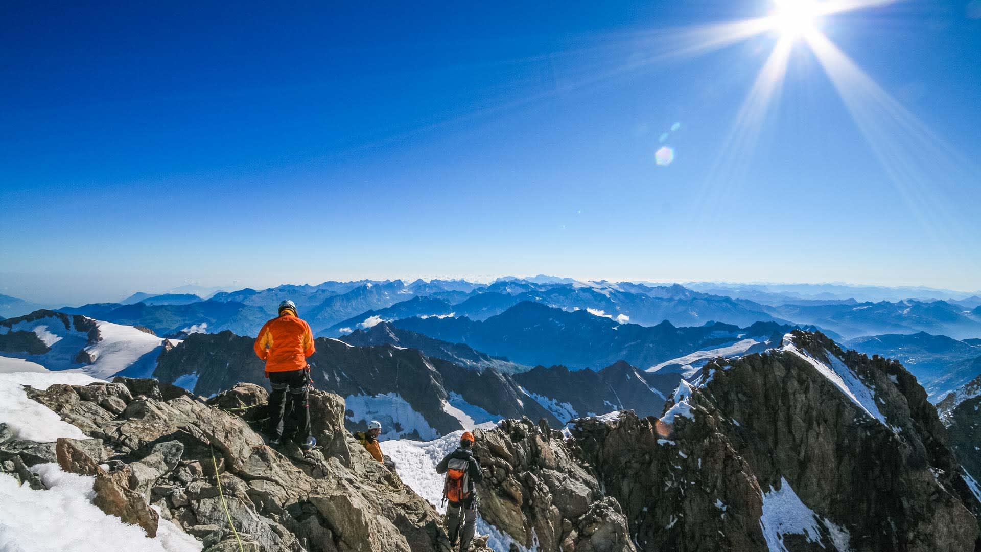 Hochtour am Schreckhorn: drei Bergsteiger mit Klettergurt und Helm auf felsigem Hochgebirgsgrat mit Restschnee.