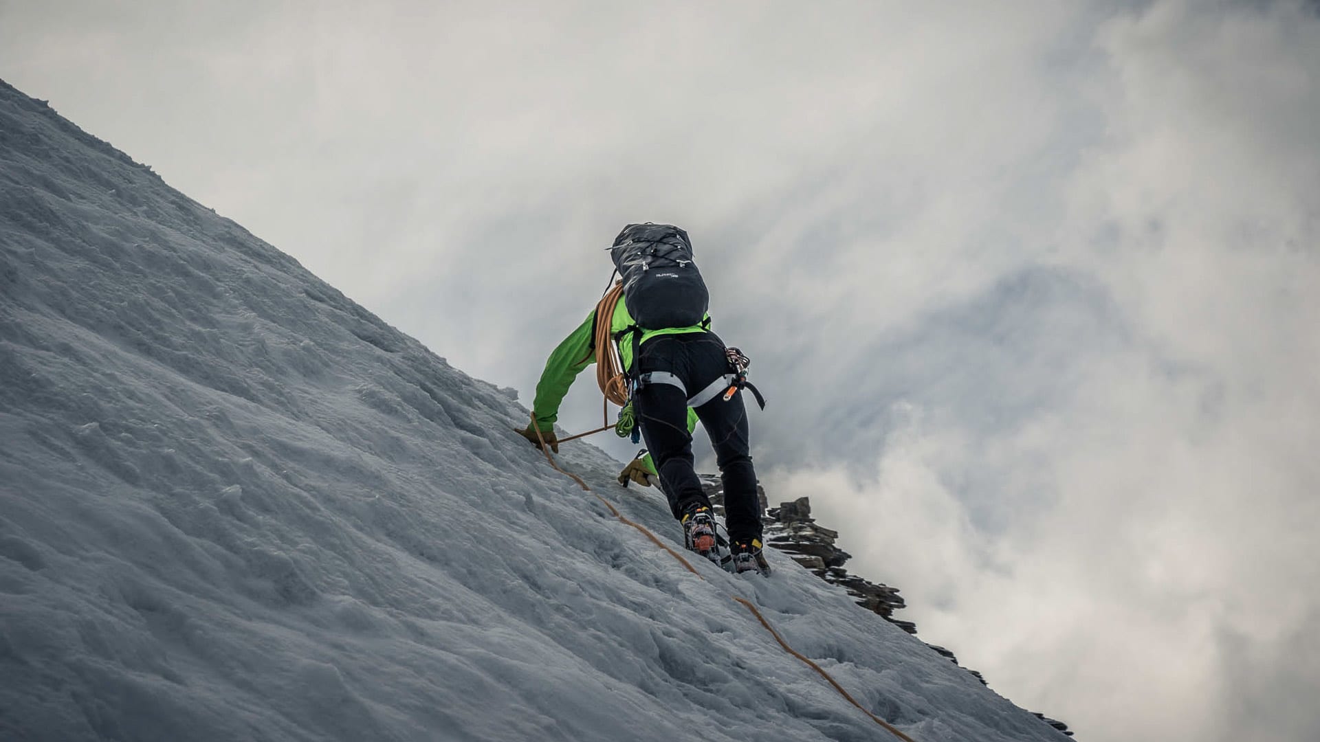 Bergsteiger klettert mit Steigeisen, Pickel und Fixseil einen steilen Eis- und Schneehang der Spaghettirunde im Wallis aufwärts.