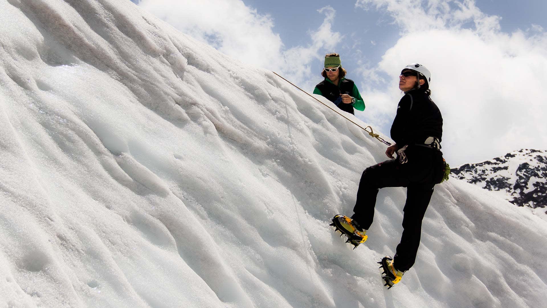 Zwei Bergsteiger üben Spaltenbergung auf einer Hochtour an einem steilen Schneefeld mit Steigeisen und Seilsicherung