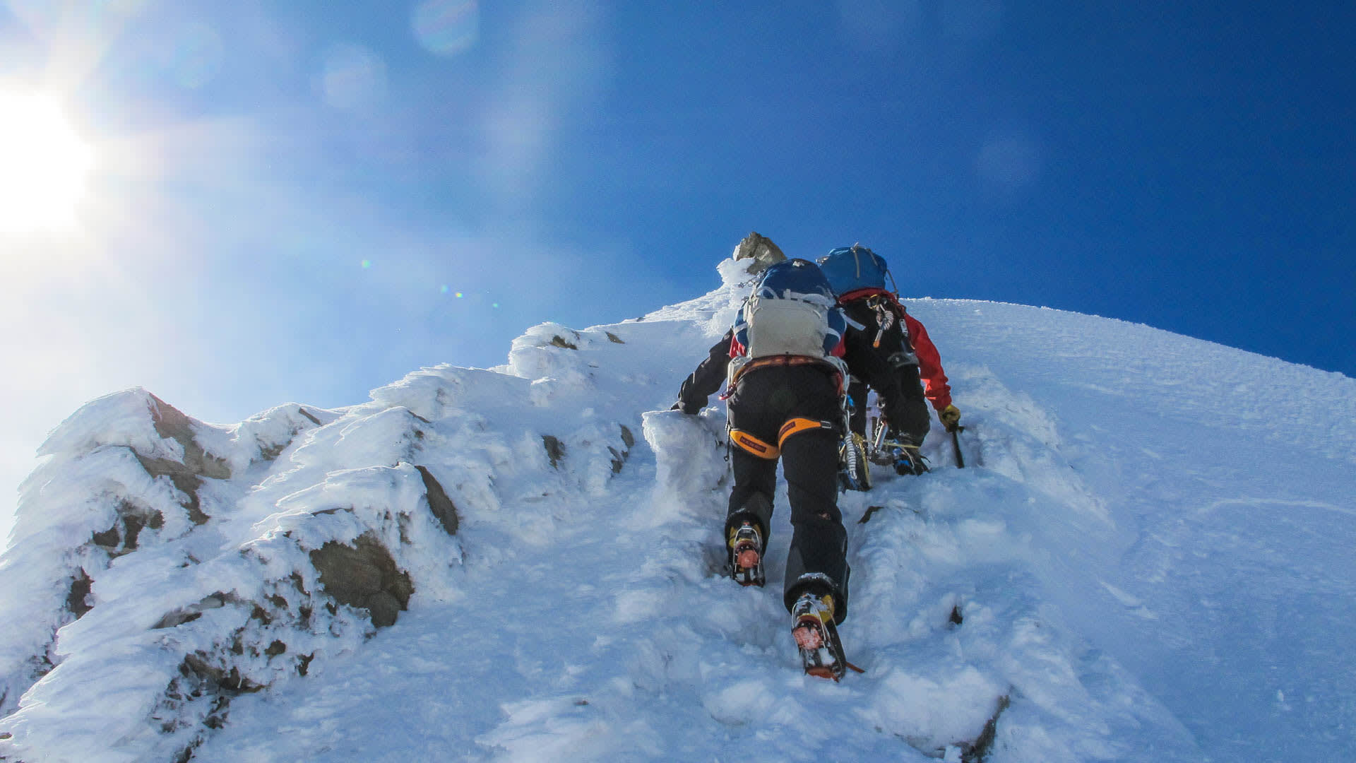 Zwei Bergsteiger mit Steigeisen und Pickel steigen den eis- und schneebedeckten Steilgrat am Piz Roseg auf.
