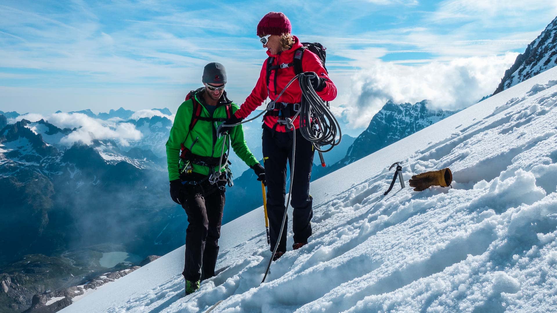 Zwei Bergsteiger mit Klettergurt und Eispickel stehen auf einem steilen Schneehang in der Schweiz.