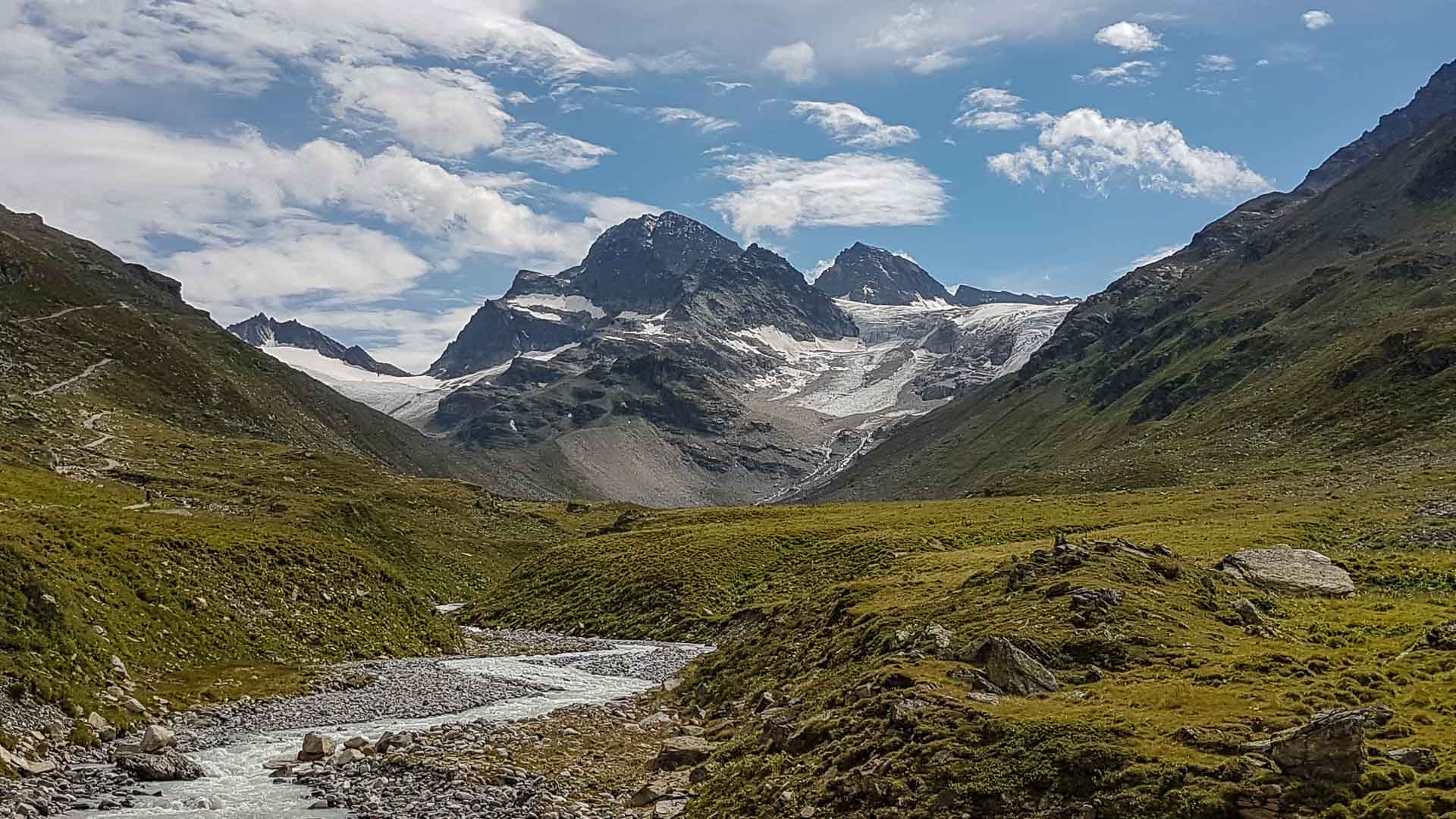 Hochtour Piz Buin: Sommerliches Hochtal mit Gletscherbach, Talwiesen und vergletschertem Felsgipfel im Hintergrund.