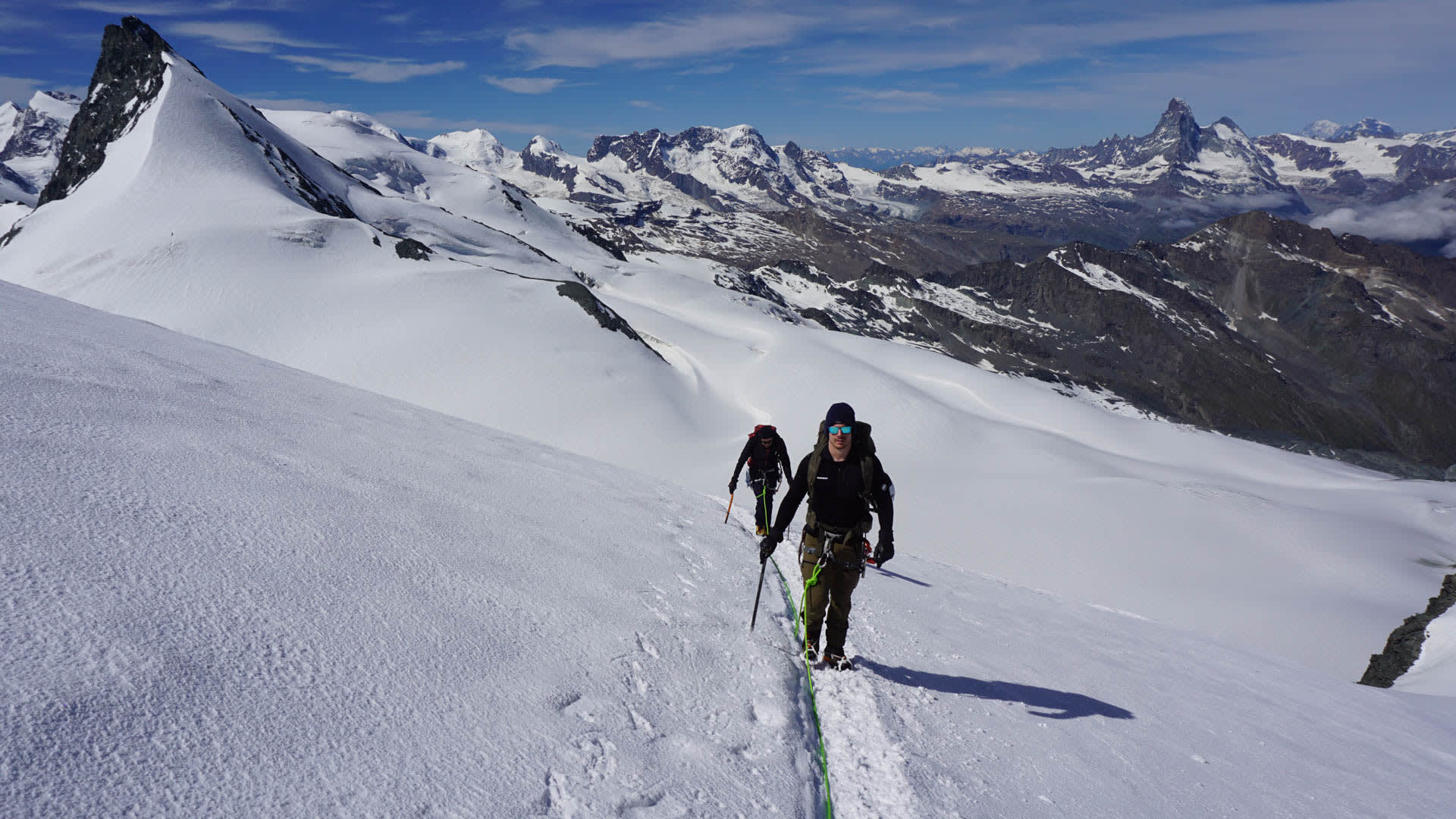 Zwei Teilnehmer eines Hochtourenkurses im Wallis steigen seilverbunden über einen schneebedeckten Gletscherhang