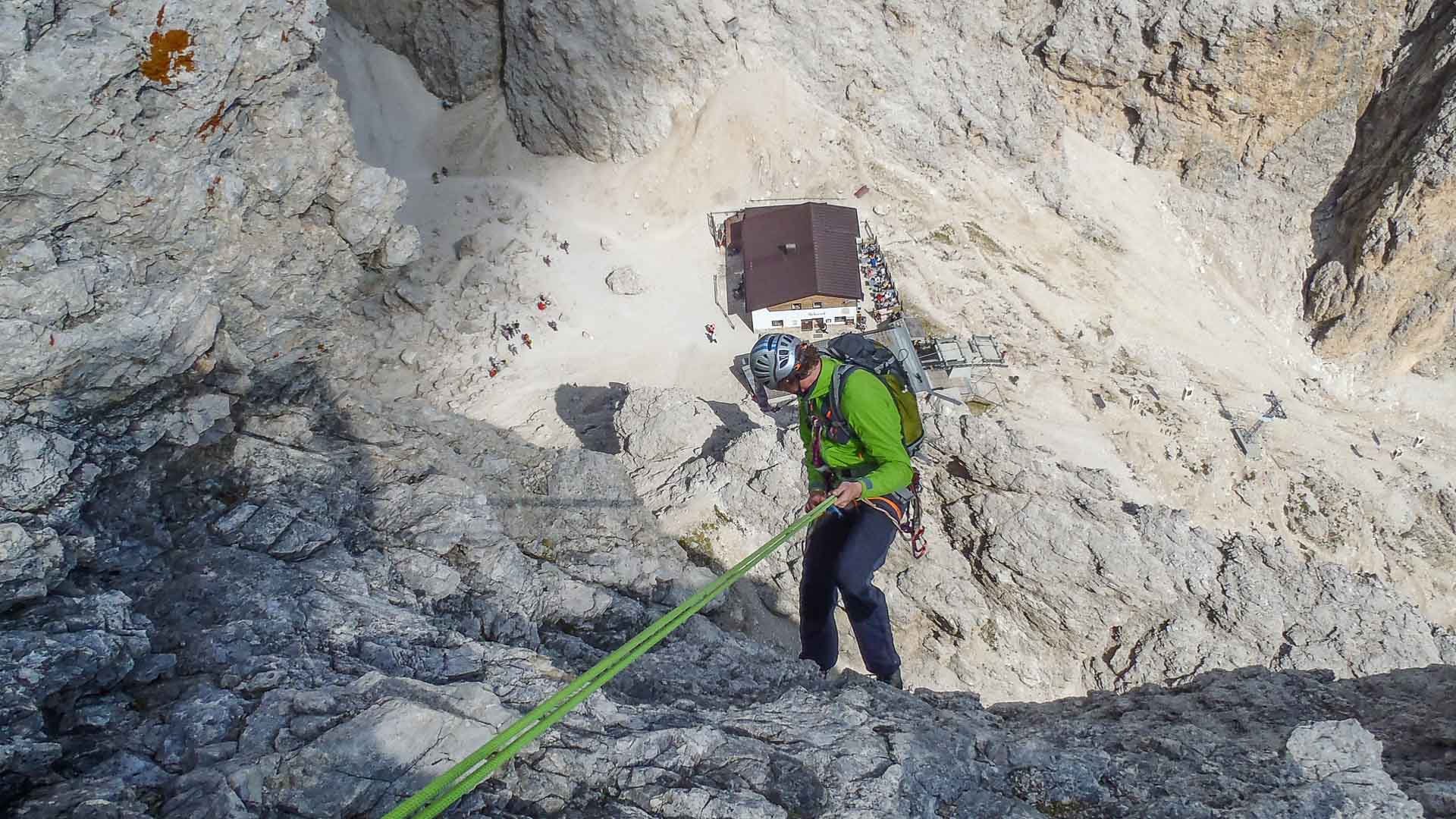 Kletterer seilt mit grünem Doppelseil, Helm und Klettergurt eine senkrechte Kalkfelswand in den Dolomiten ab.
