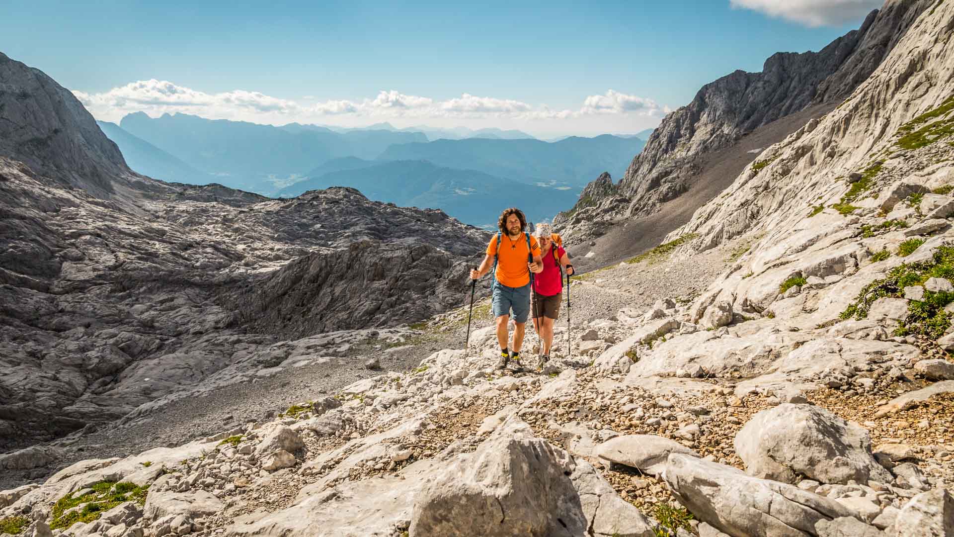 Zwei Bergsteiger steigen auf einem felsigen Schotterpfad vom Hohen Göll Richtung Berchtesgaden ab.