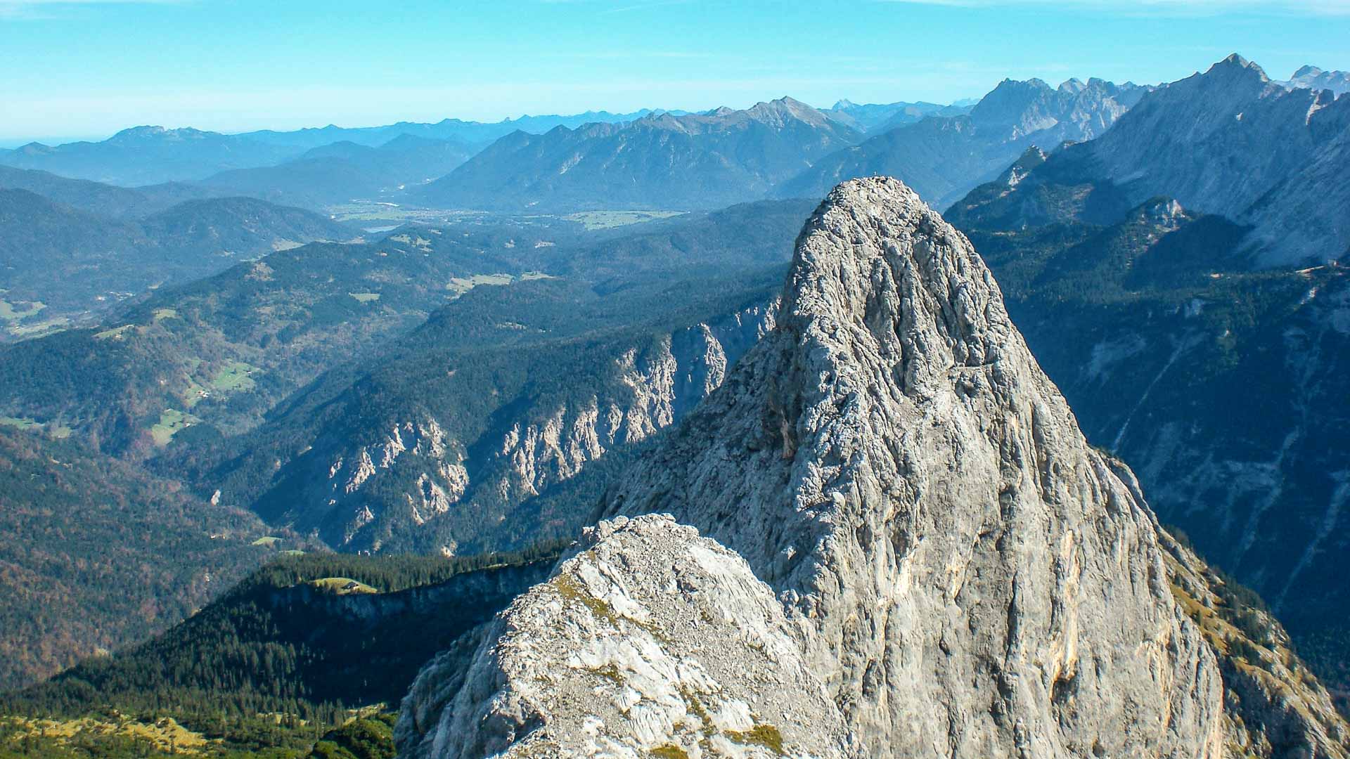 Klettern am Blassengrat: Kalkfelsgipfel der Zugspitze über herbstlich verfärbtem Gebirgstal mit kleinem See im Hintergrund.