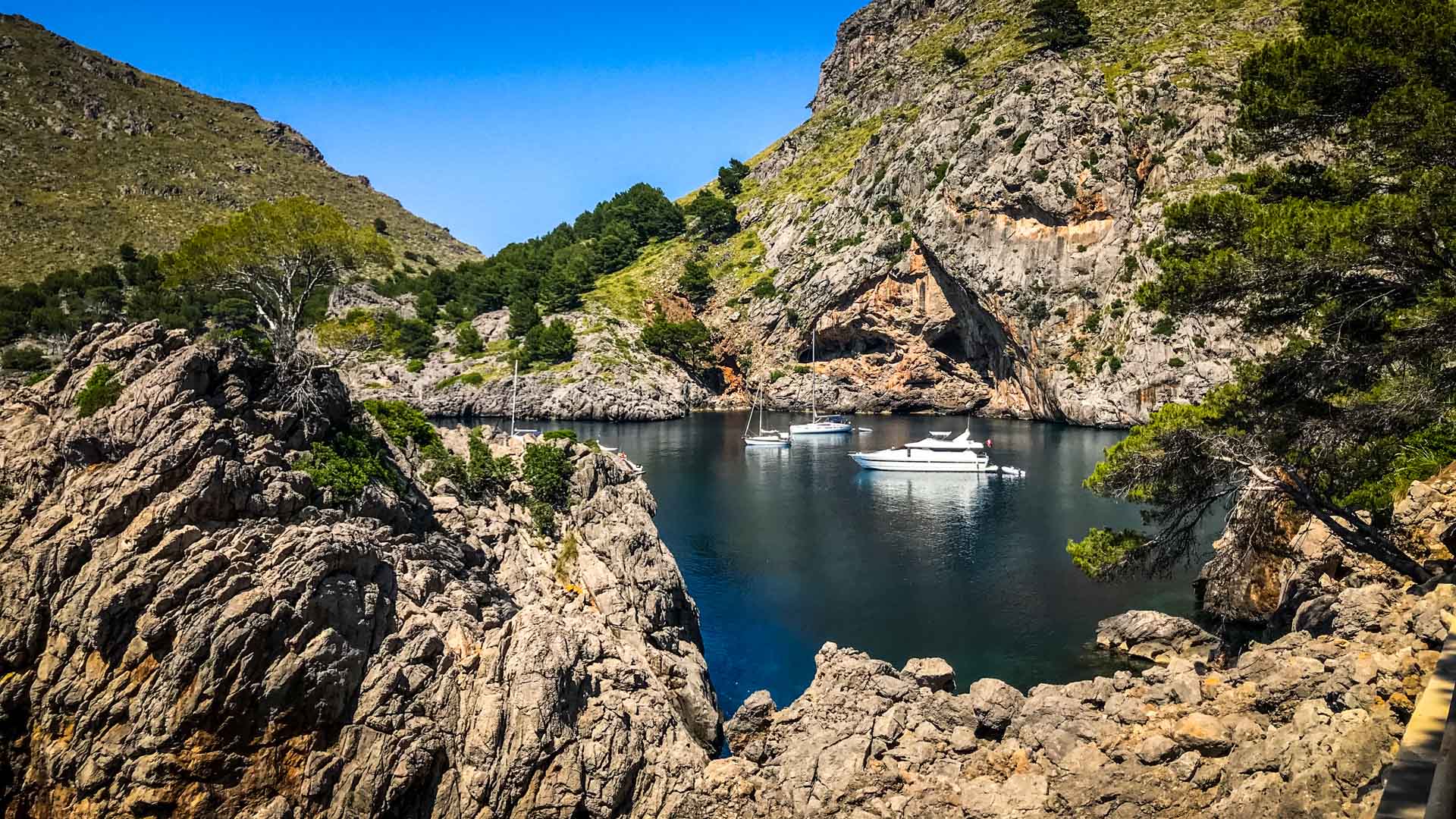 Kleine Cala auf Mallorca mit türkisblauem Wasser, weißen Booten und steilen Kalksteinfelsen der Serra de Tramuntana.