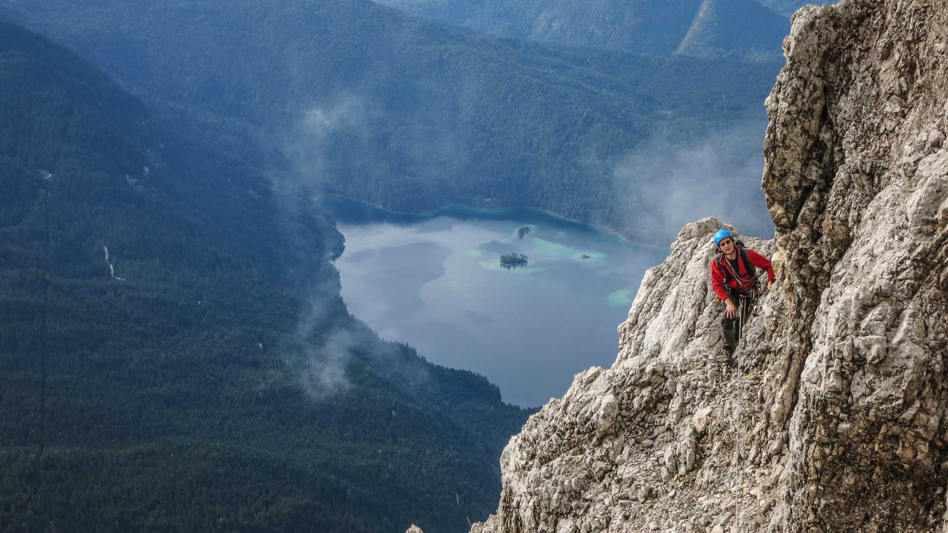Klettern in der Eisenzeit über dem Eibsee: Kletterer mit blauem Helm und roter Jacke an steiler Kalkwand
