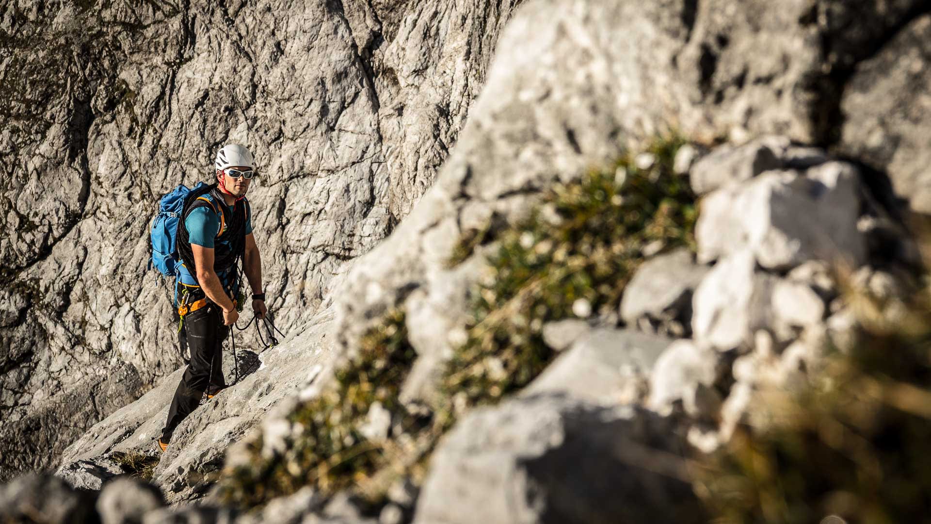 Kletterer mit Helm und Klettergurt steigt über eine Kalkfelsplatte im zweiten Drittel der Watzmann Ostwand kurz