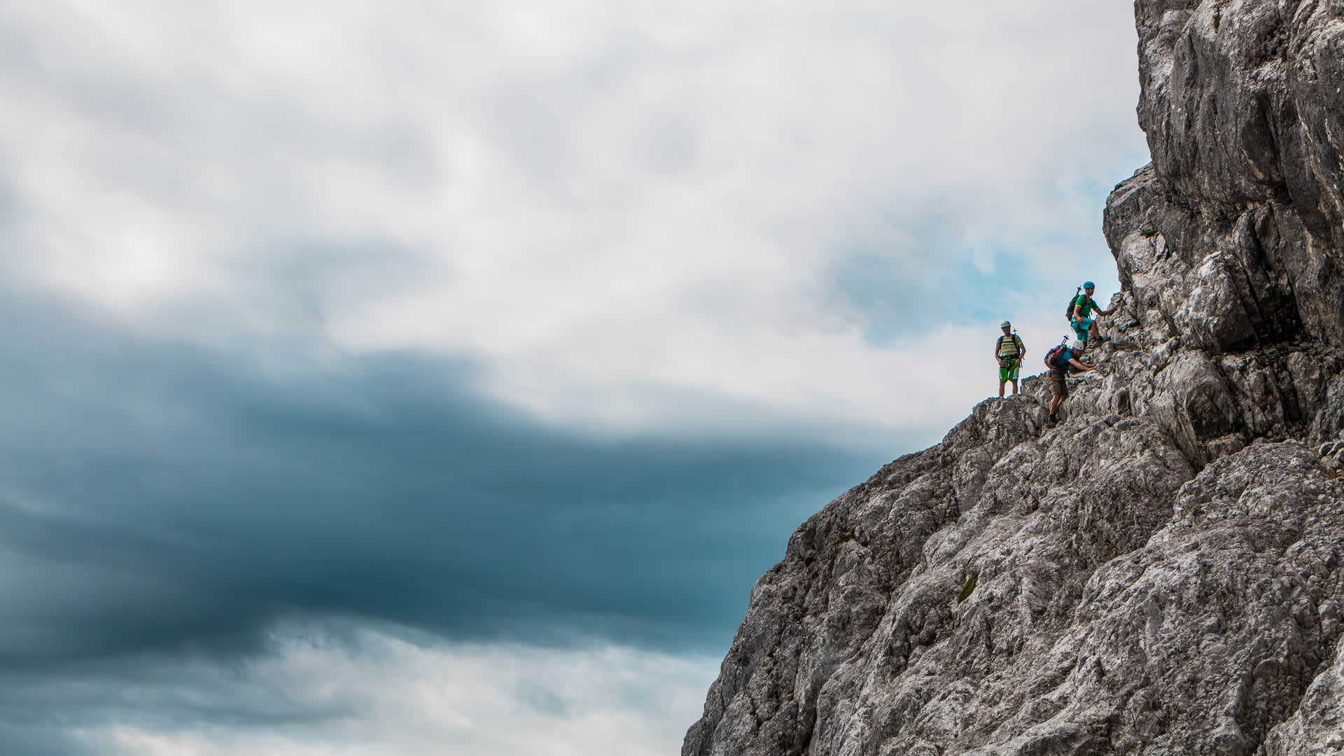 Drei Kletterer stehen und sichern auf schmalem Felsband in der steilen Hochwanner Nordwand bei bewölktem Himmel.
