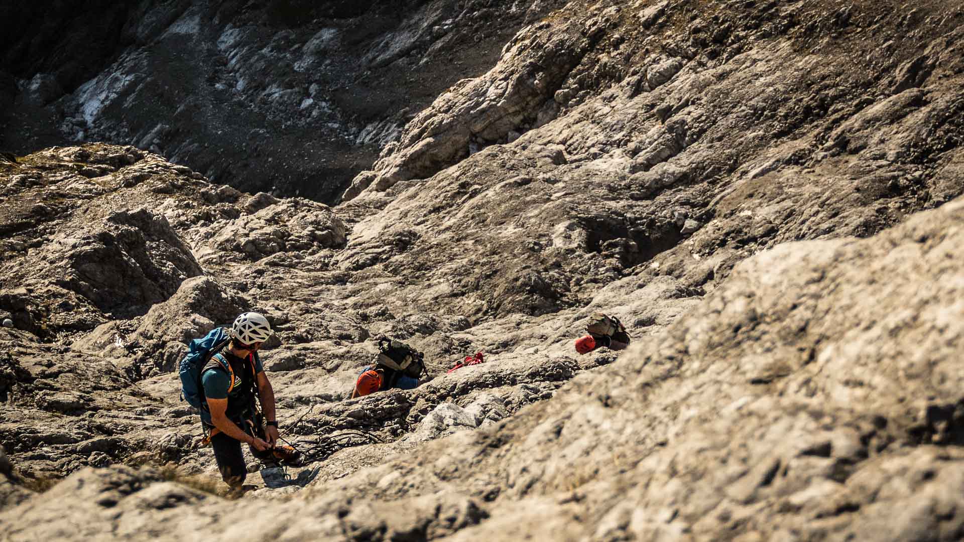 Drei Kletterer mit Helmen und Rucksäcken steigen eine schräge Kalkfelsplatte in der Watzmann Ostwand auf.