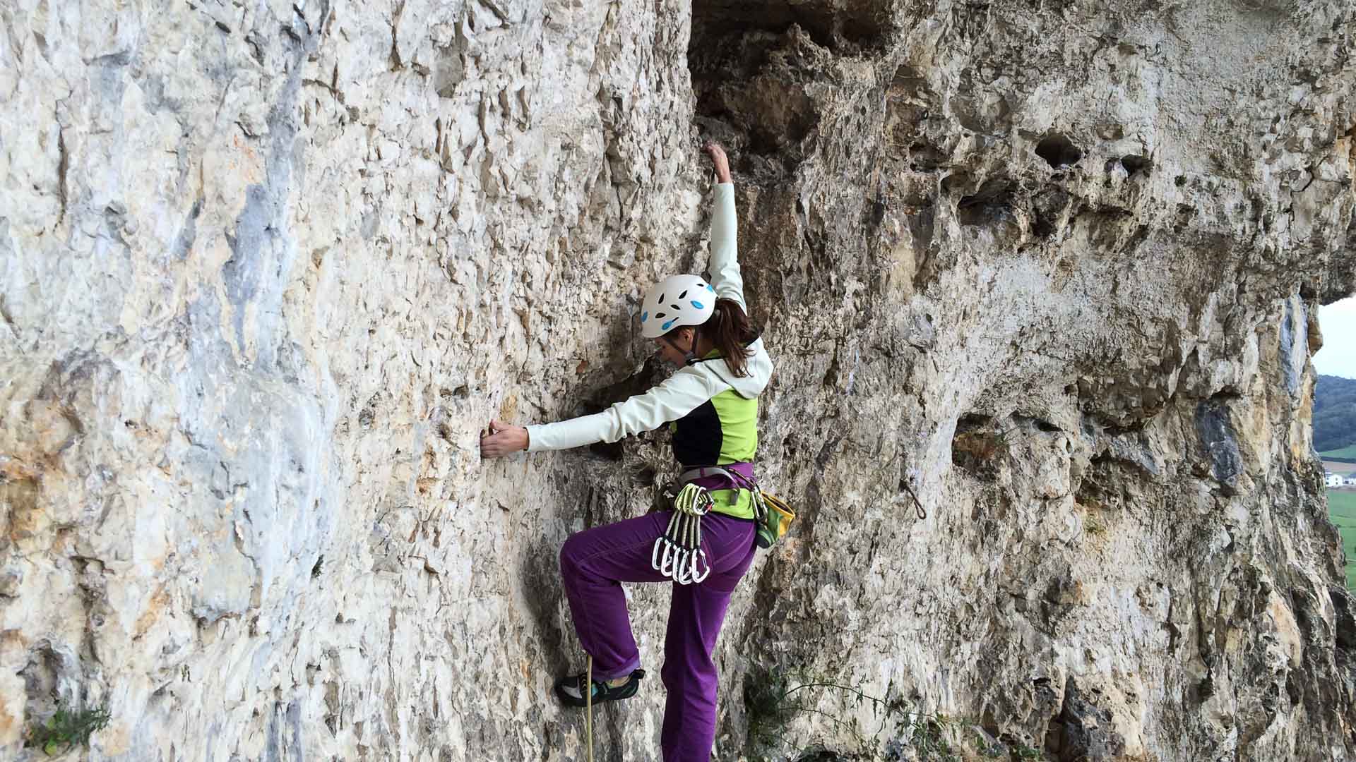 Person klettert mit weißem Helm und Kletterseil an senkrechter Kalksteinwand im Blautal der Schwäbischen Alb.