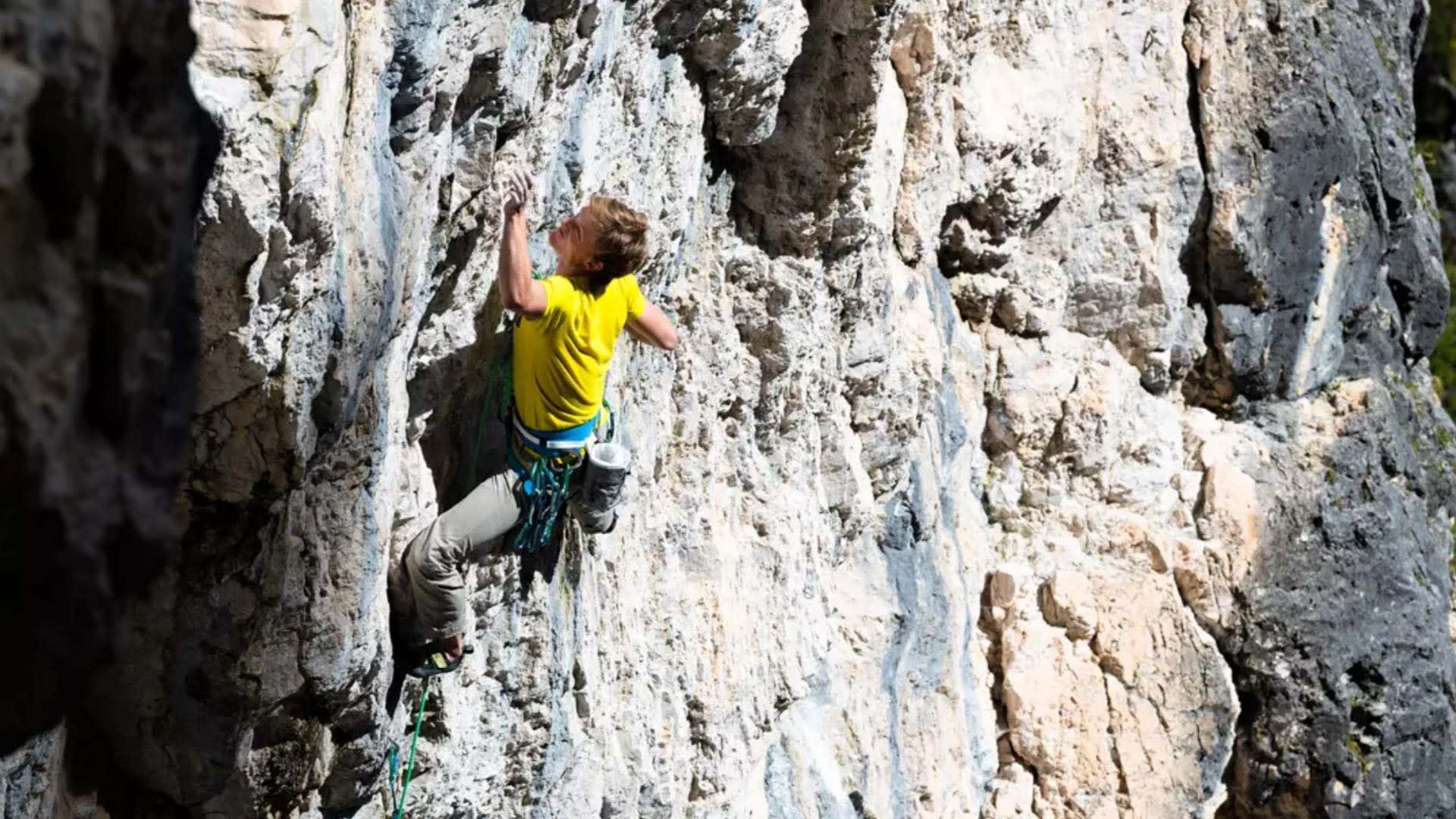Nahaufnahme eines Kletterers mit gelbem T-Shirt, Klettergurt und Expressen an heller Kalksteinwand bei den Drei Zinnen.