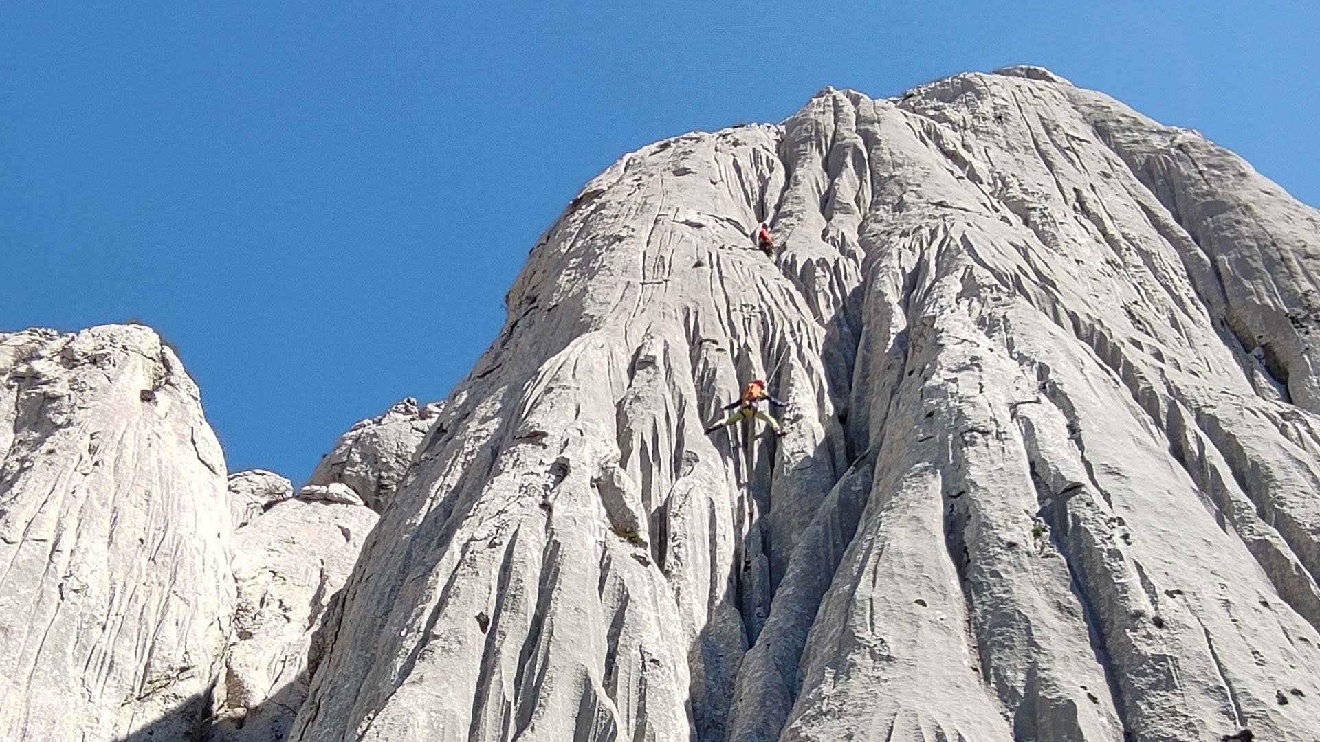 Zwei Kletterer an einer steilen, gerillten Kalksteinwand in der Paklenica unter blauem Himmel.