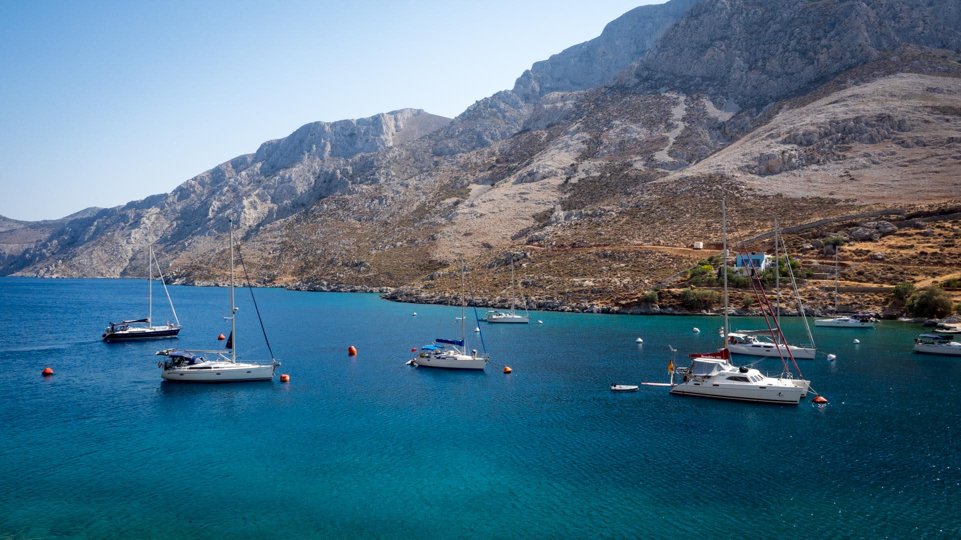 Ankerbucht auf Kalymnos mit Segelbooten im türkisblauen Wasser und steilem Kalkfelsen – Kletterrevier der Insel im Sommer.