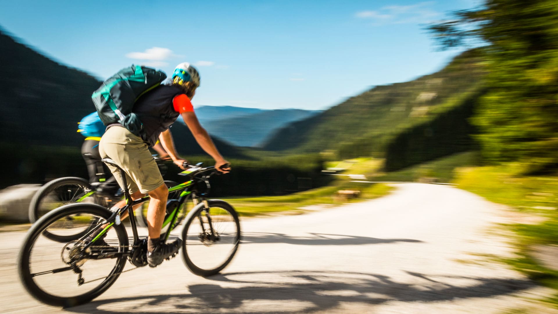 Zwei Mountainbiker fahren per E-Bike den Zustieg zur Klettertour am Watzmann in den Berchtesgadener Alpen auf einem Schotterweg