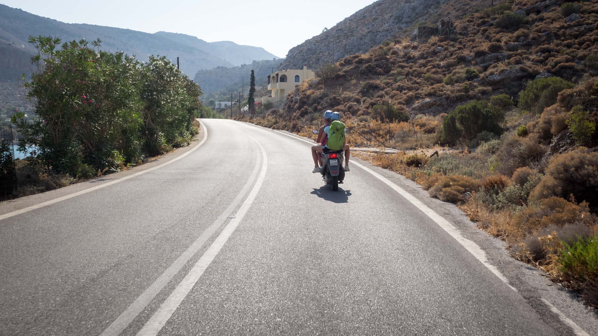 Zwei Kletterer fahren auf einem Motorroller durch die trockene Hügellandschaft von Kalymnos zur Klettertour.
