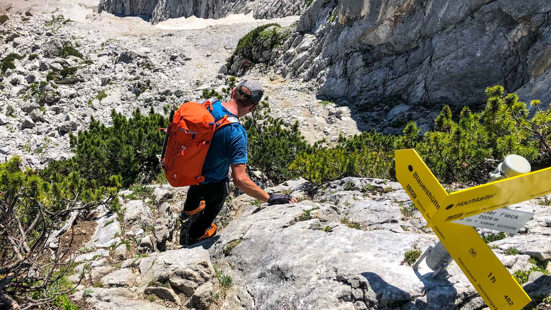 Kletterer steigt auf Kalkfels am Roter Fleck auf, Wegweiser zur Blaueishütte und Hochkalter im Vordergrund, Berchtesgadener Alpen.