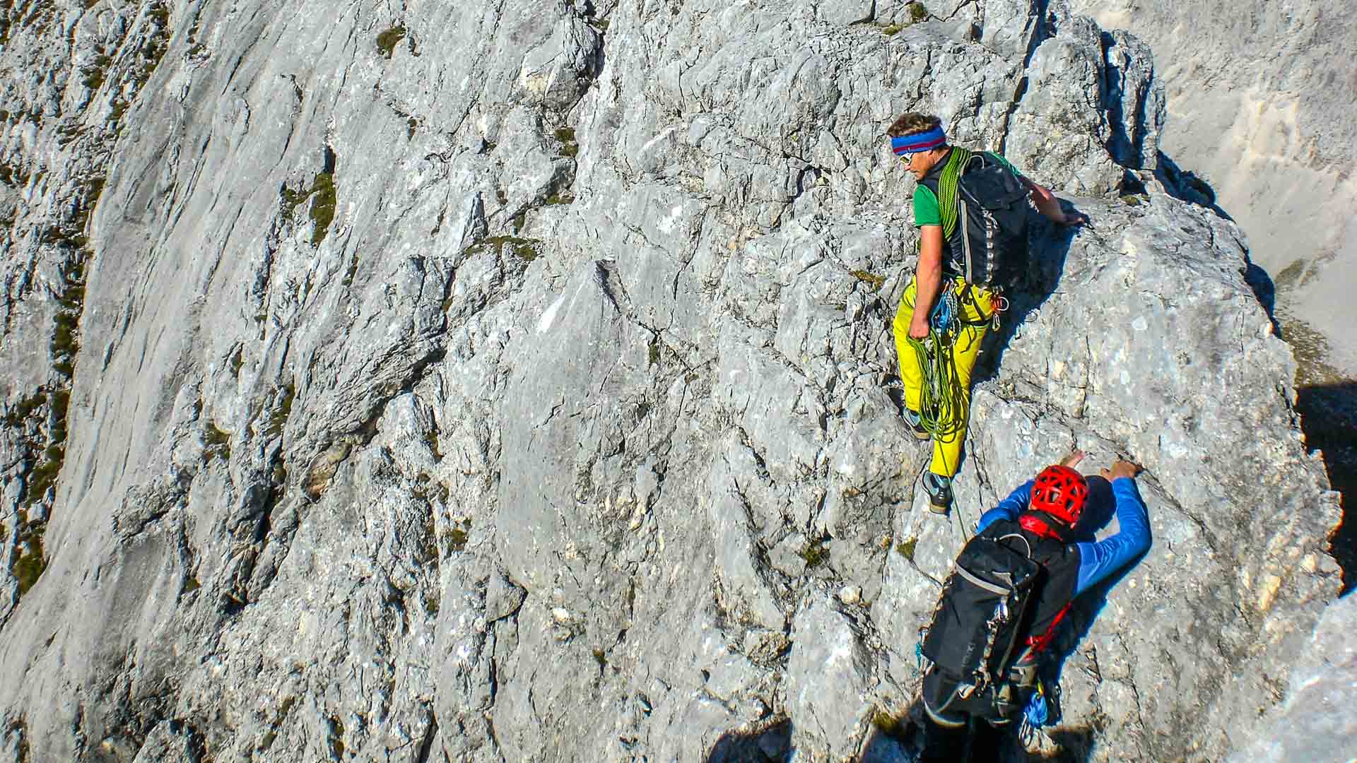 Klettern am Blassengrat: zwei Kletterer mit Gurt und Seil in steiler Kalkfelswand, Sicherungsposition von oben fotografiert.