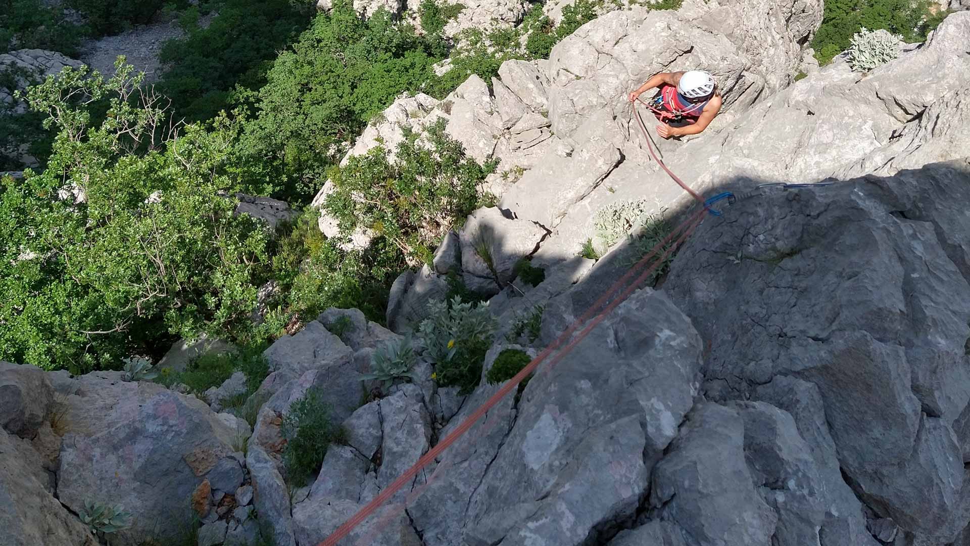 Kletterin sichert am Standplatz in Paklenica einen Nachsteiger mit rotem Seil an steiler Kalksteinwand.