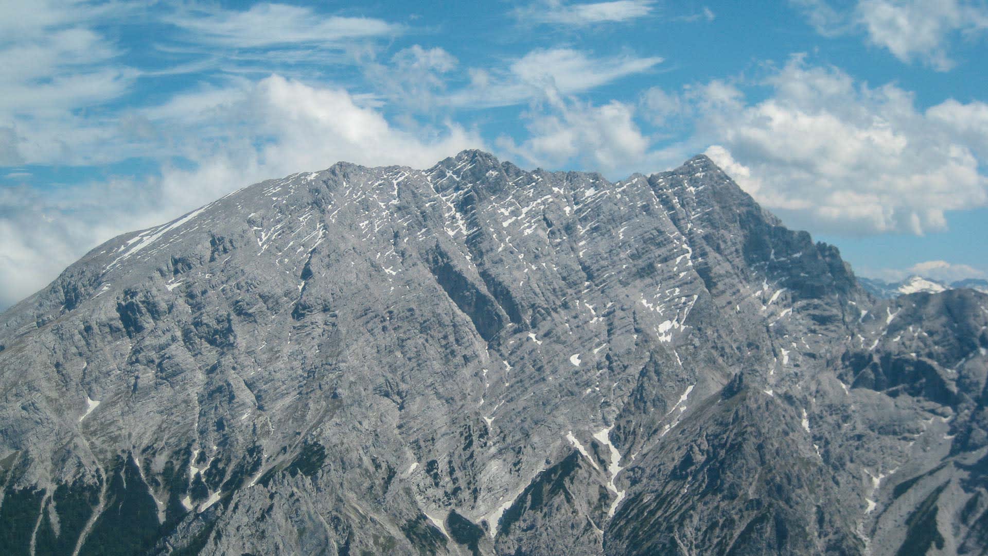 Felswand des Watzmann mit senkrechten Kalksteinschrofen, Schneeresten und gezacktem Grat in den Berchtesgadener Alpen.